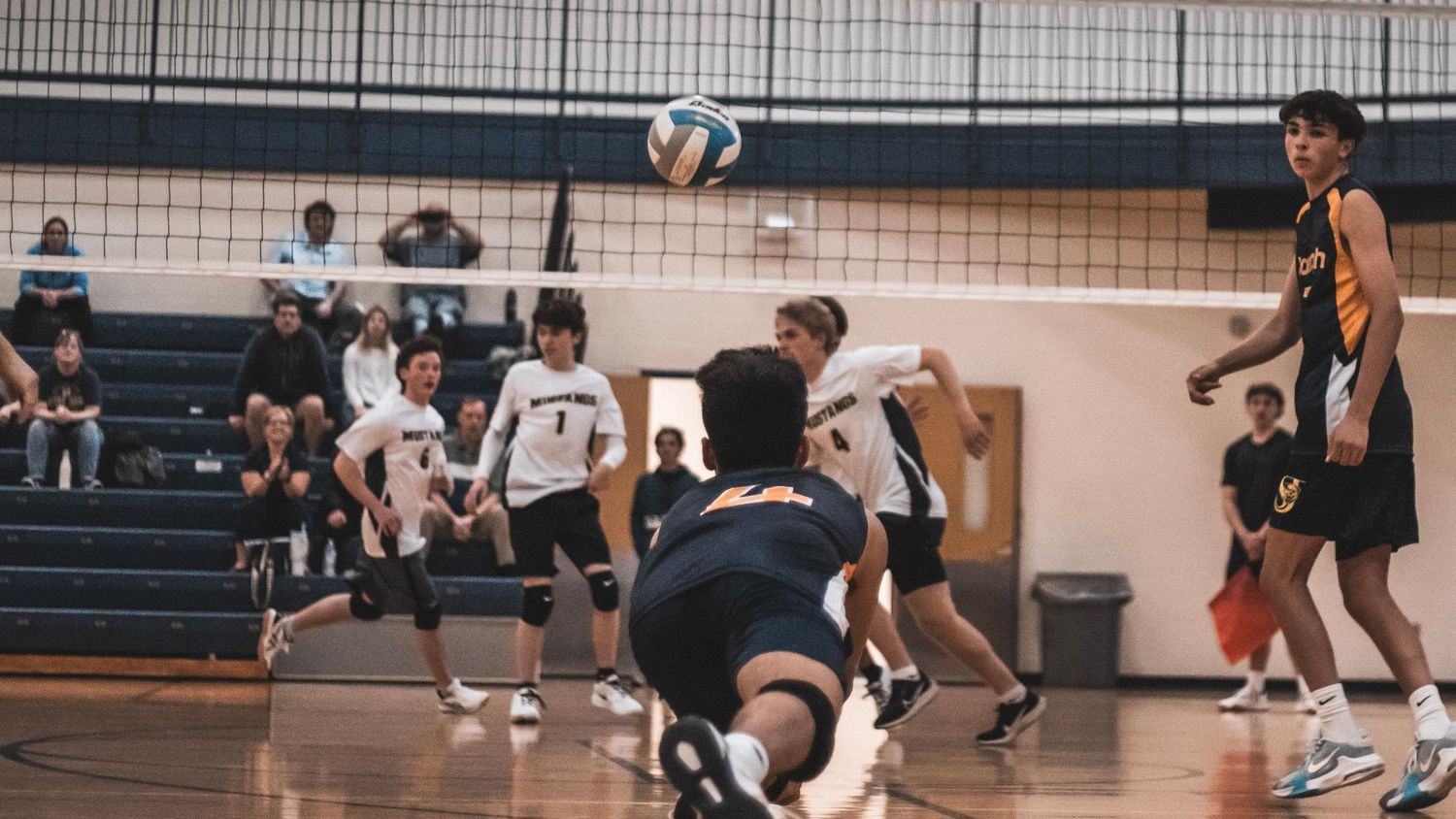 Indoor volleyball match with players actively positioning during gameplay.