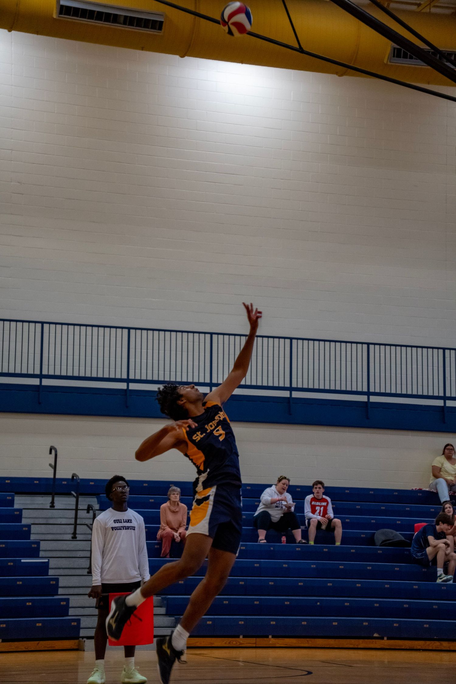 Player reaches high to spike volleyball during competitive indoor match.