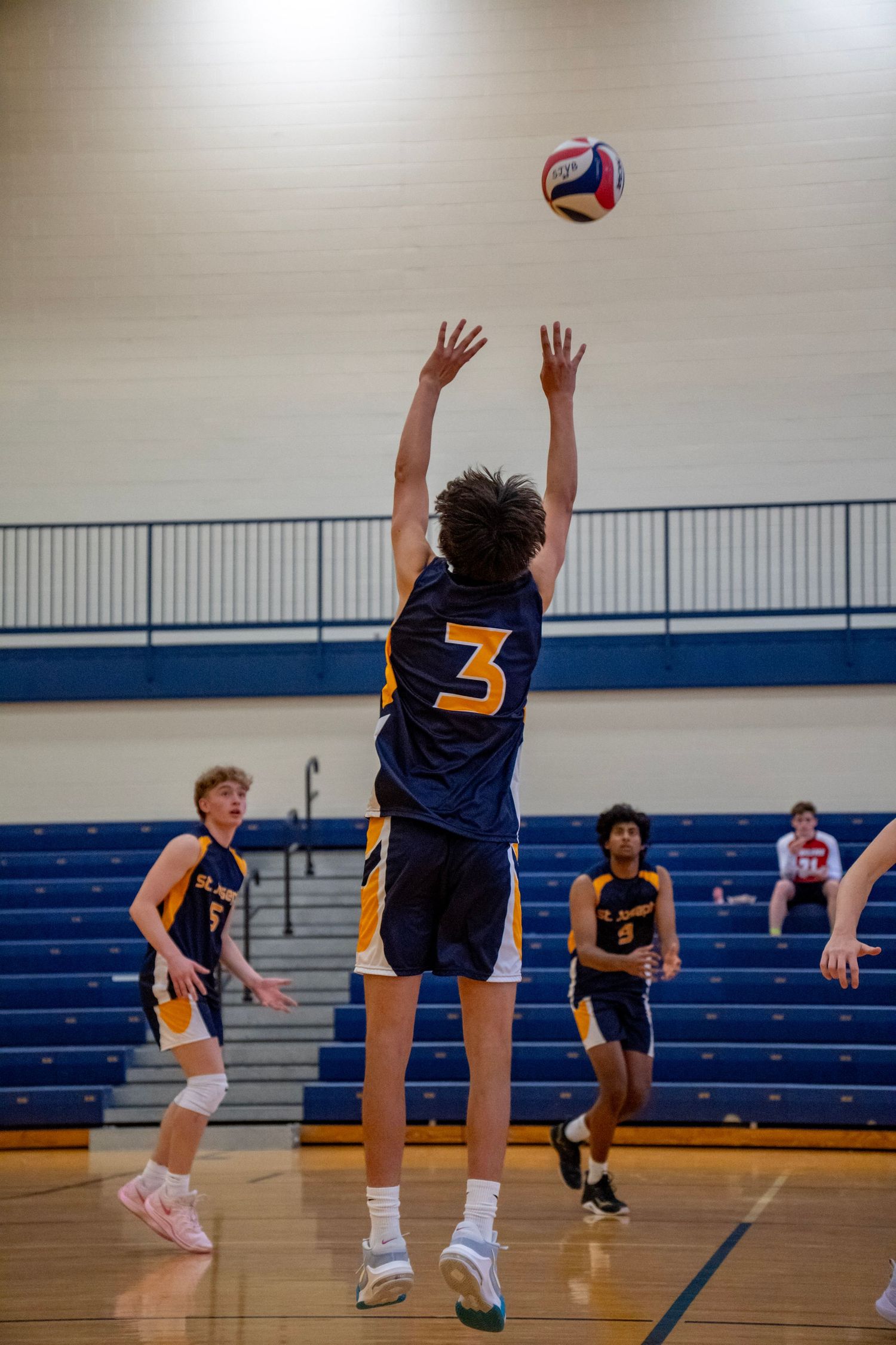 Player in navy jersey number 3 jumping to block a volleyball during a match.
