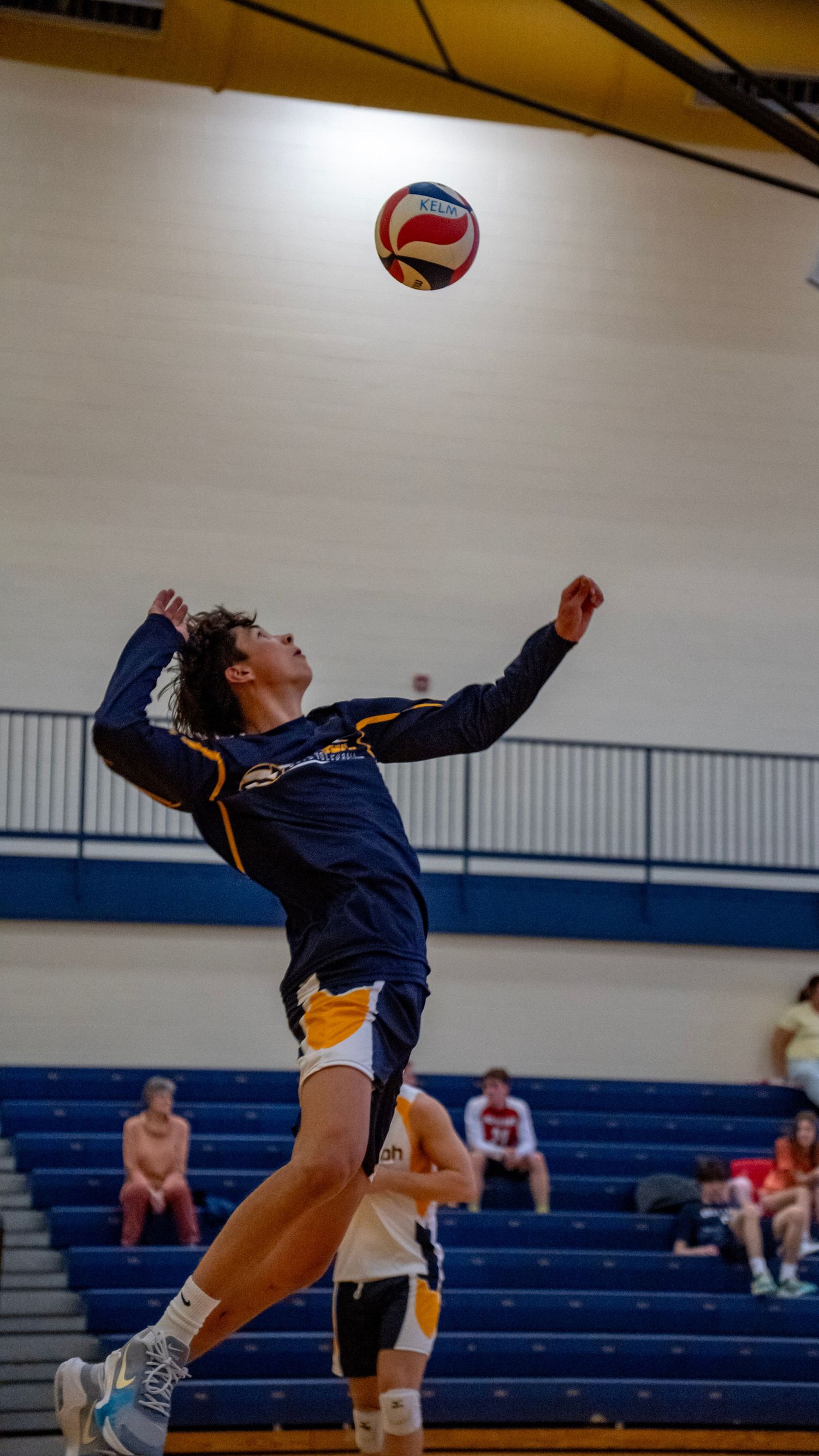 Player in navy uniform extends backwards to serve during a volleyball match.