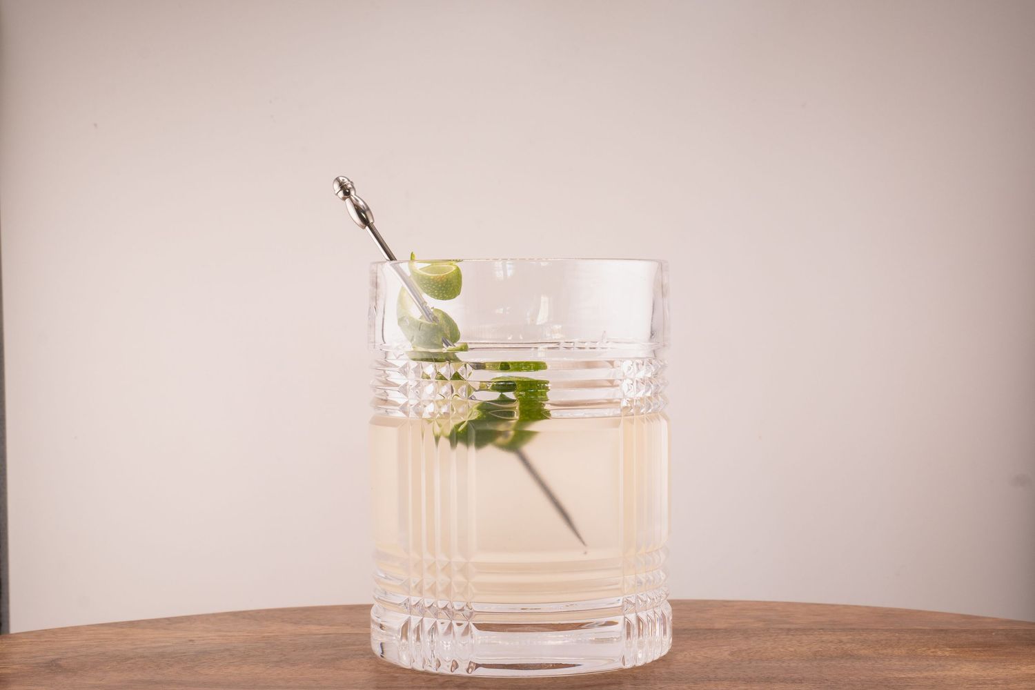 Clear cocktail with fresh herb garnish served in cut crystal rocks glass on wooden table.
