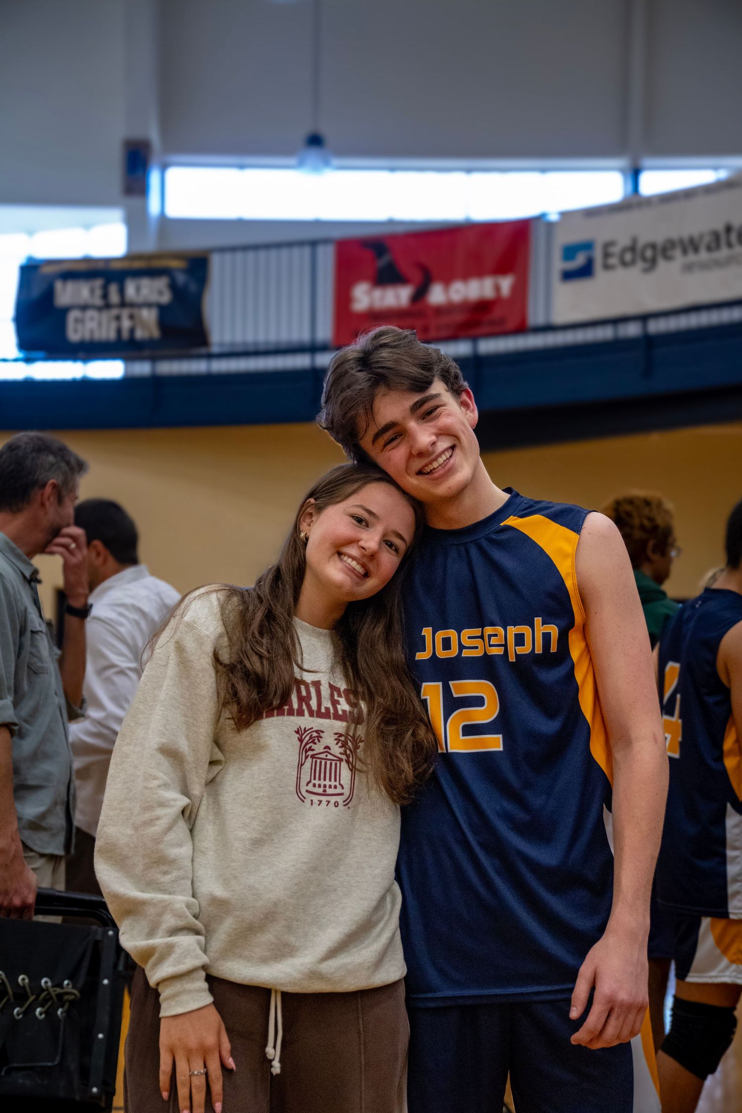 Two students smile while posing together in a school gymnasium.