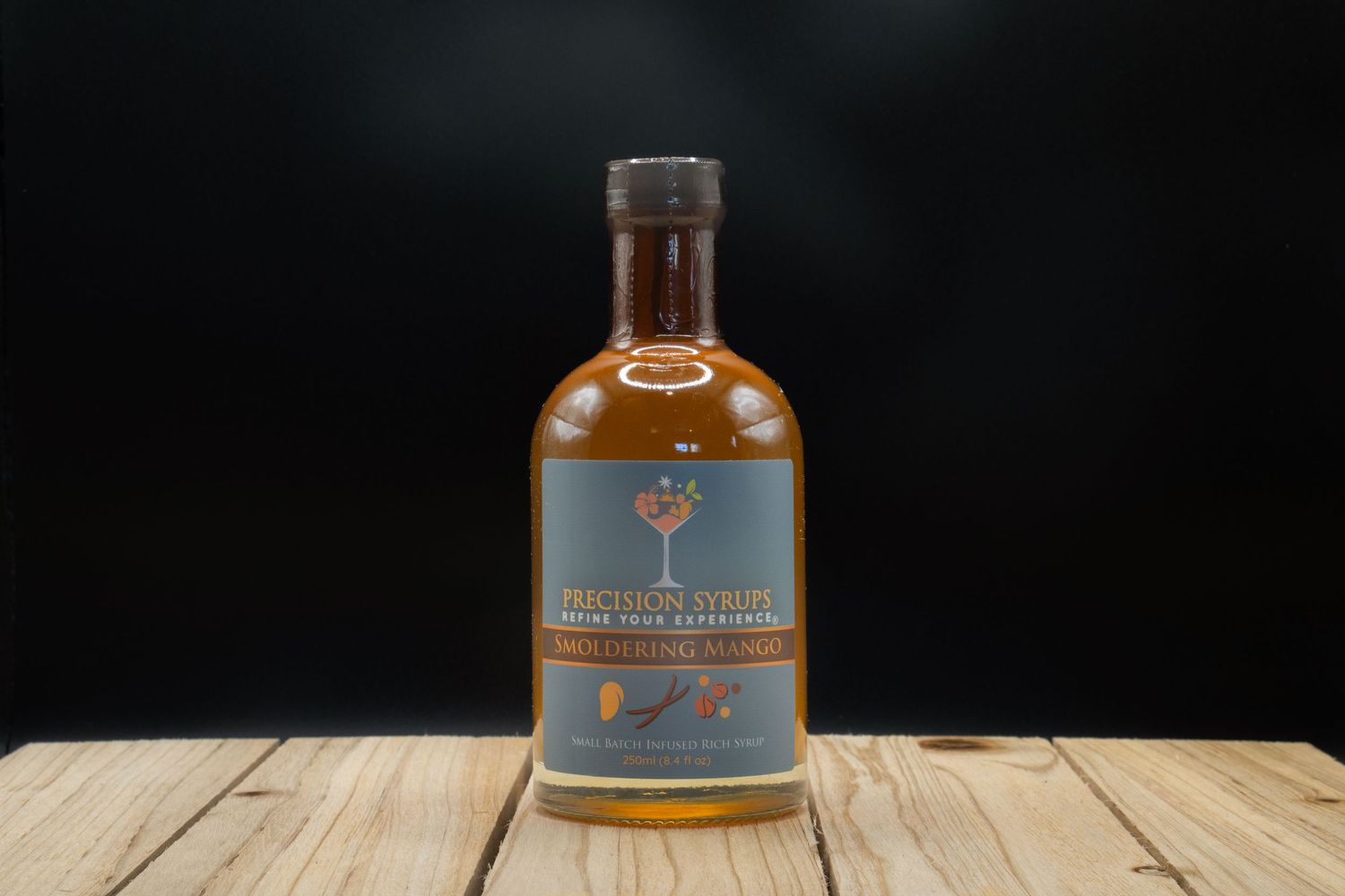 Amber-colored spirits bottle with tree logo photographed on wooden surface against dark background.
