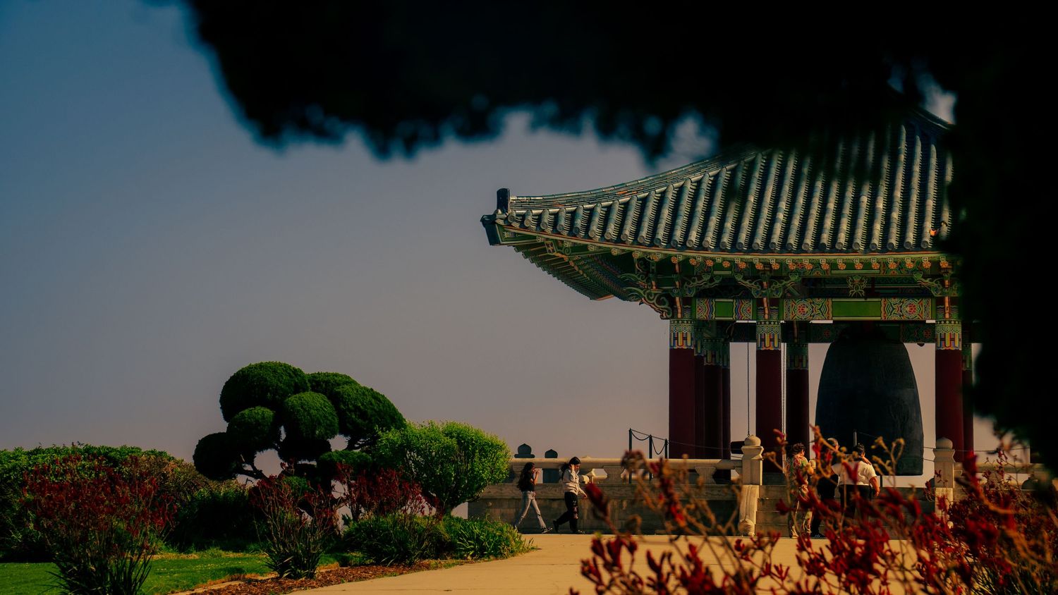 A panoramic view of a Korean-style pavilion and gardens with ornate architecture against a blue sky.