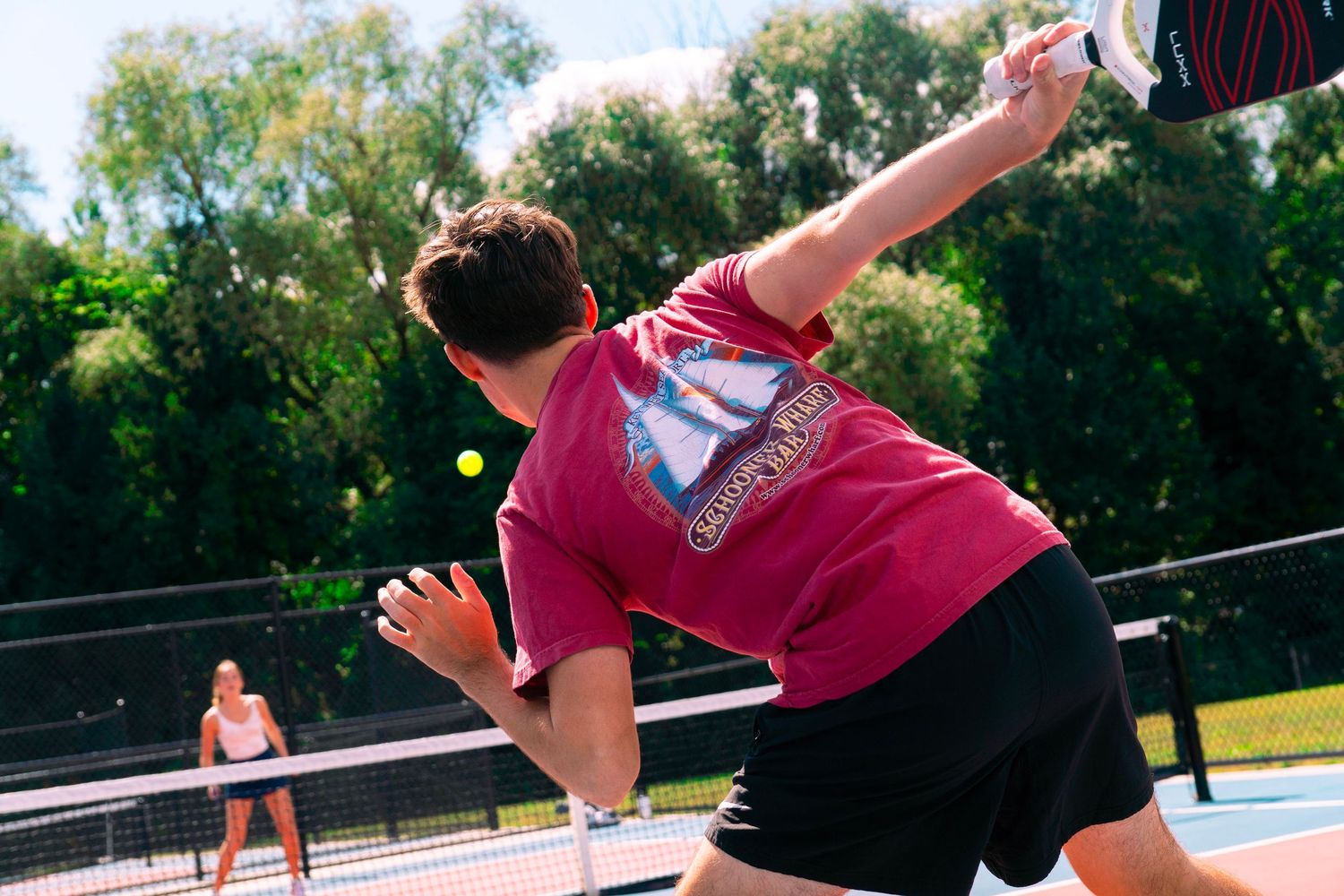 A gymnast soars through the air while performing a backflip on an outdoor trampoline in a sunny backyard setting.