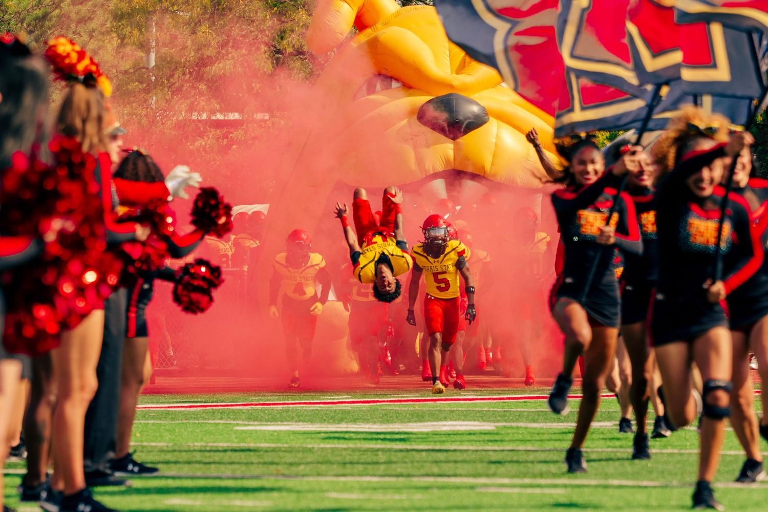 Football players run onto the field through red smoke during a dramatic game entrance celebration.