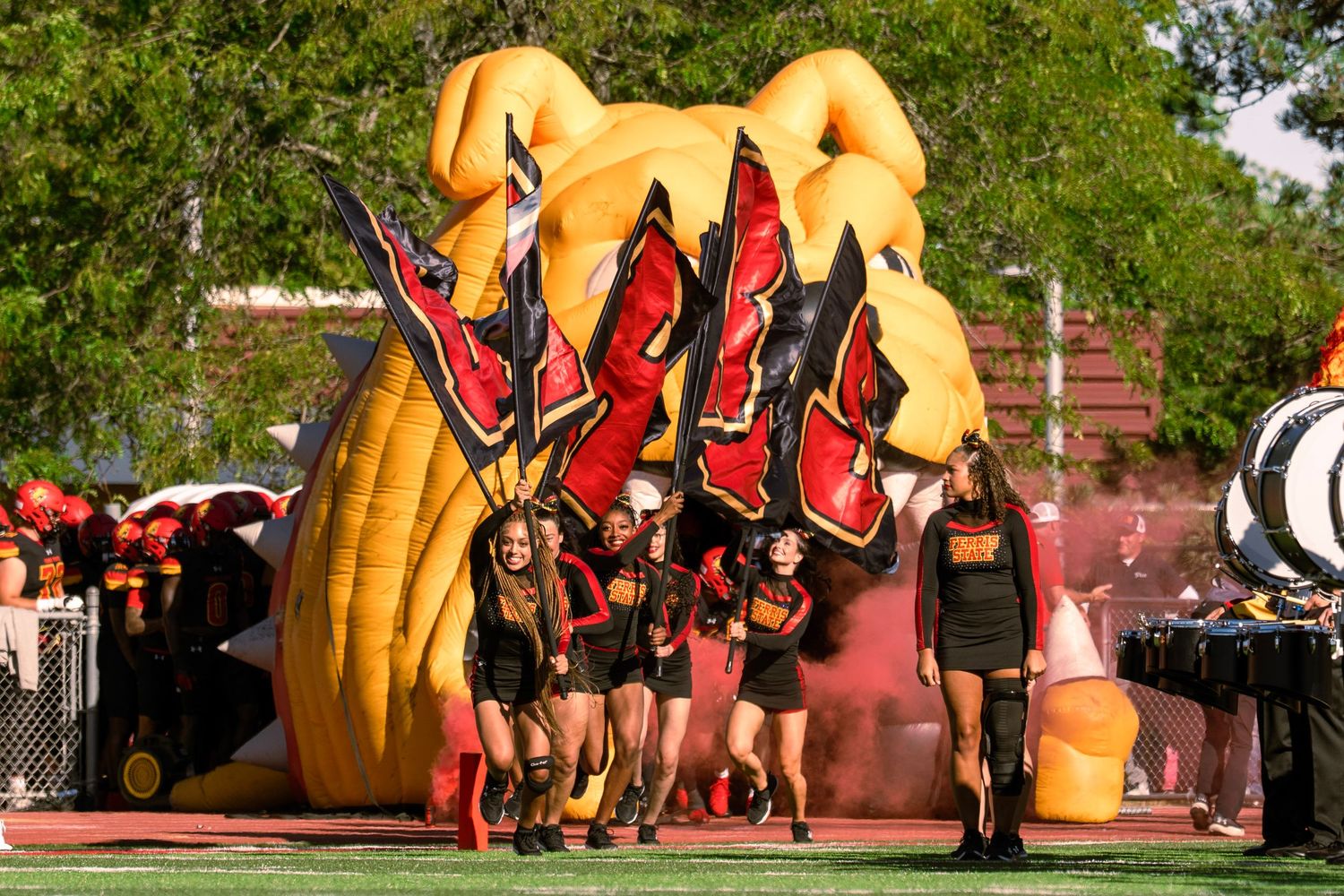 Sports team poses in front of a large yellow inflatable mascot at an outdoor campus event.