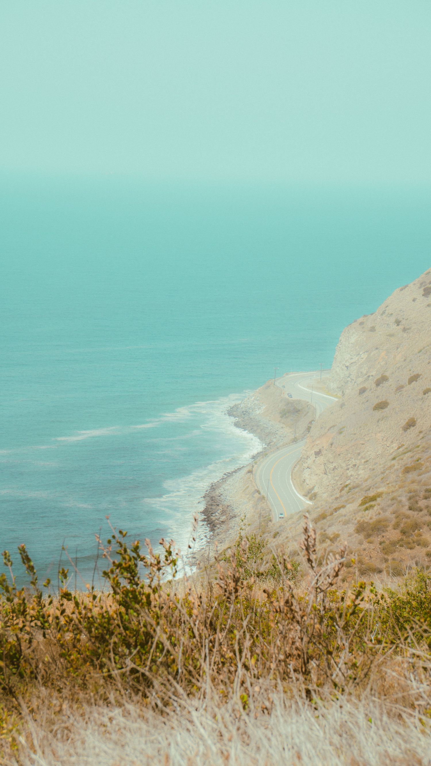 Scenic coastal highway winding along rugged cliffs beside the turquoise Pacific Ocean.
