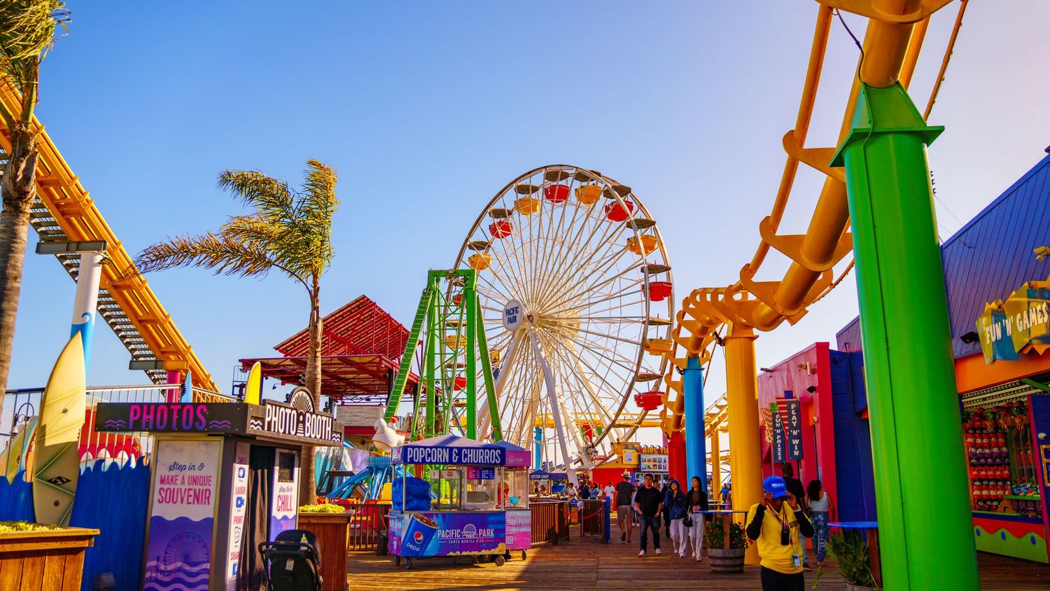 Wide panorama of an amusement park showing multiple rides and attractions under a bright blue sky.