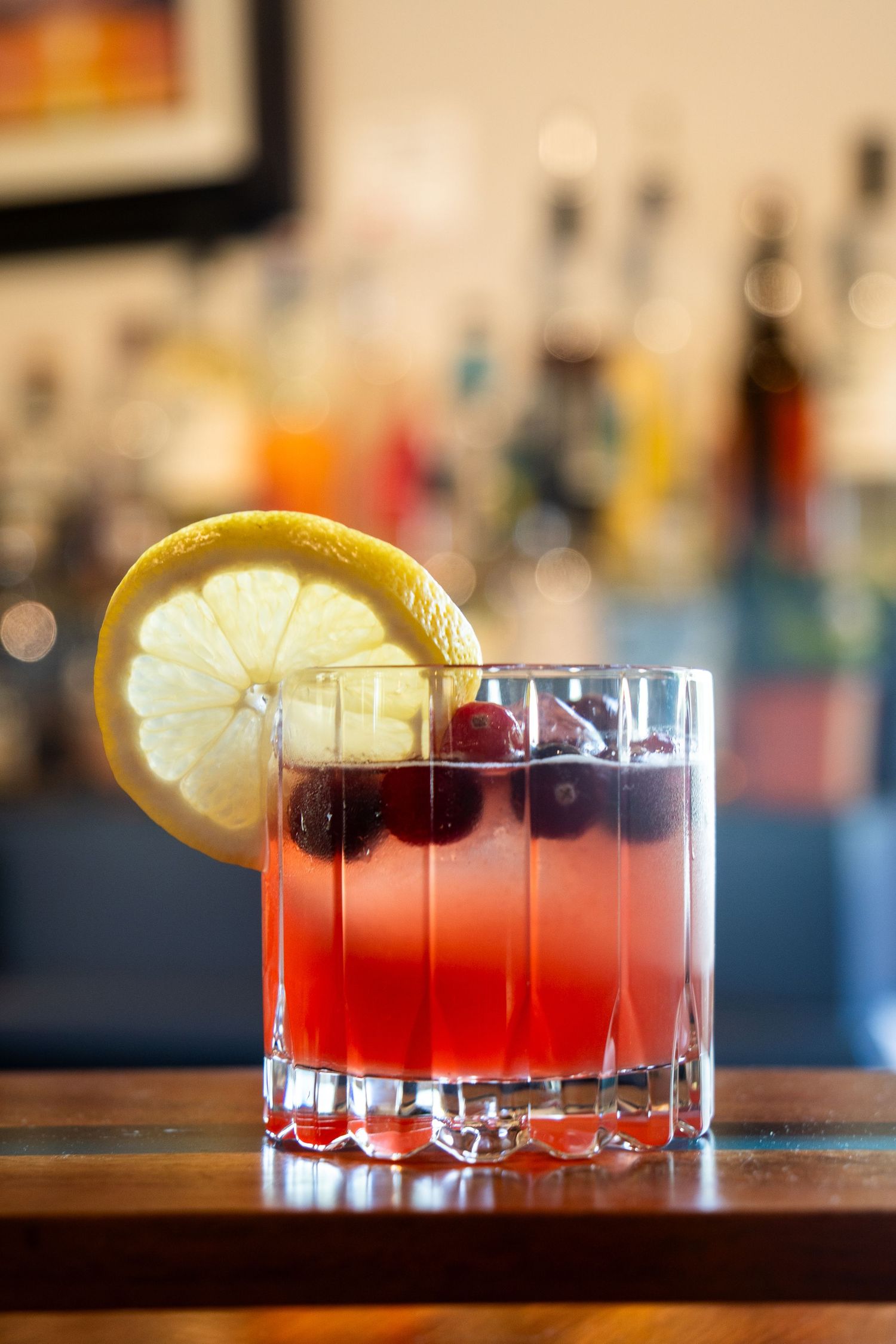 Line of red cocktails with citrus garnish on dark bar counter.