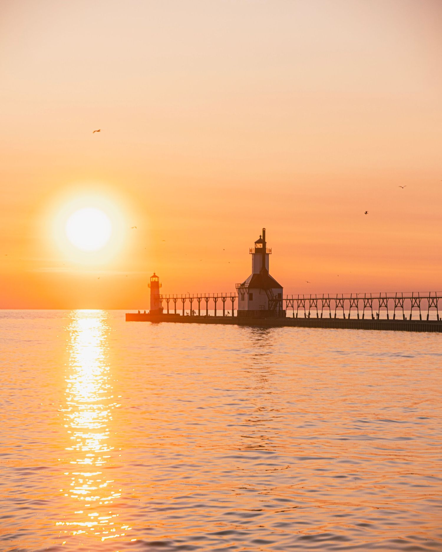 Twin lighthouses stand guard at pier entrance during spectacular golden hour sunset.
