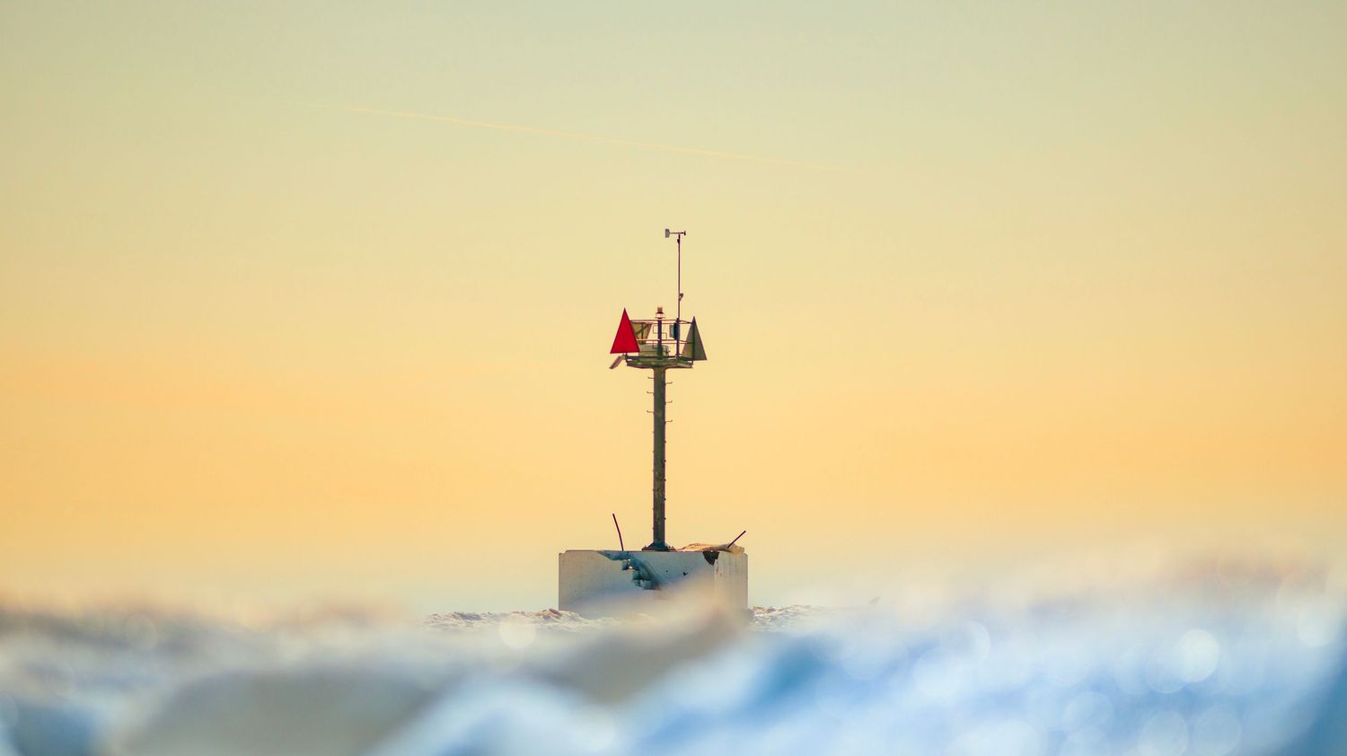 Maritime navigation marker emerging through misty ocean waves at sunrise.