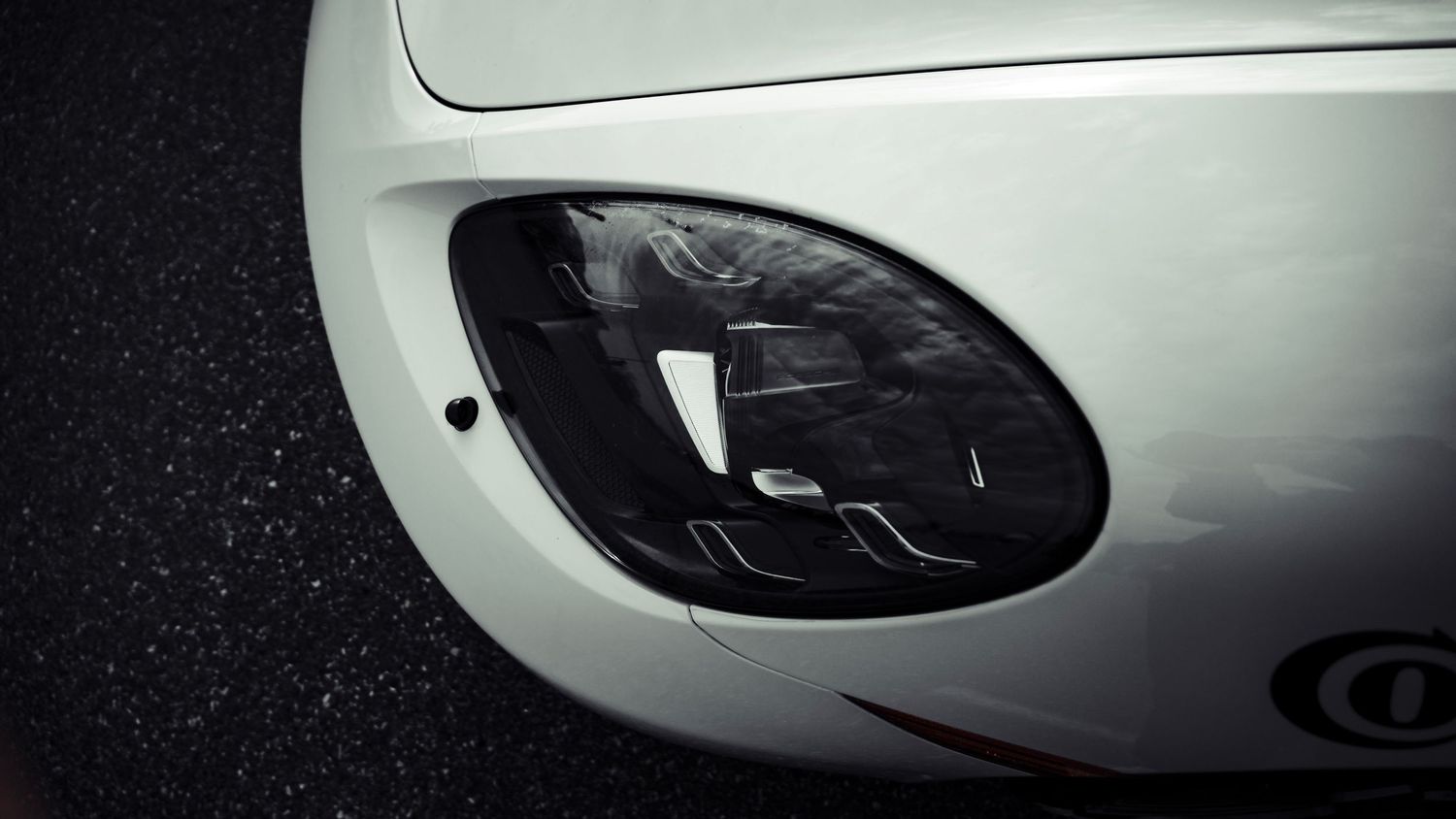 Close-up of white race car headlight with black housing detail.