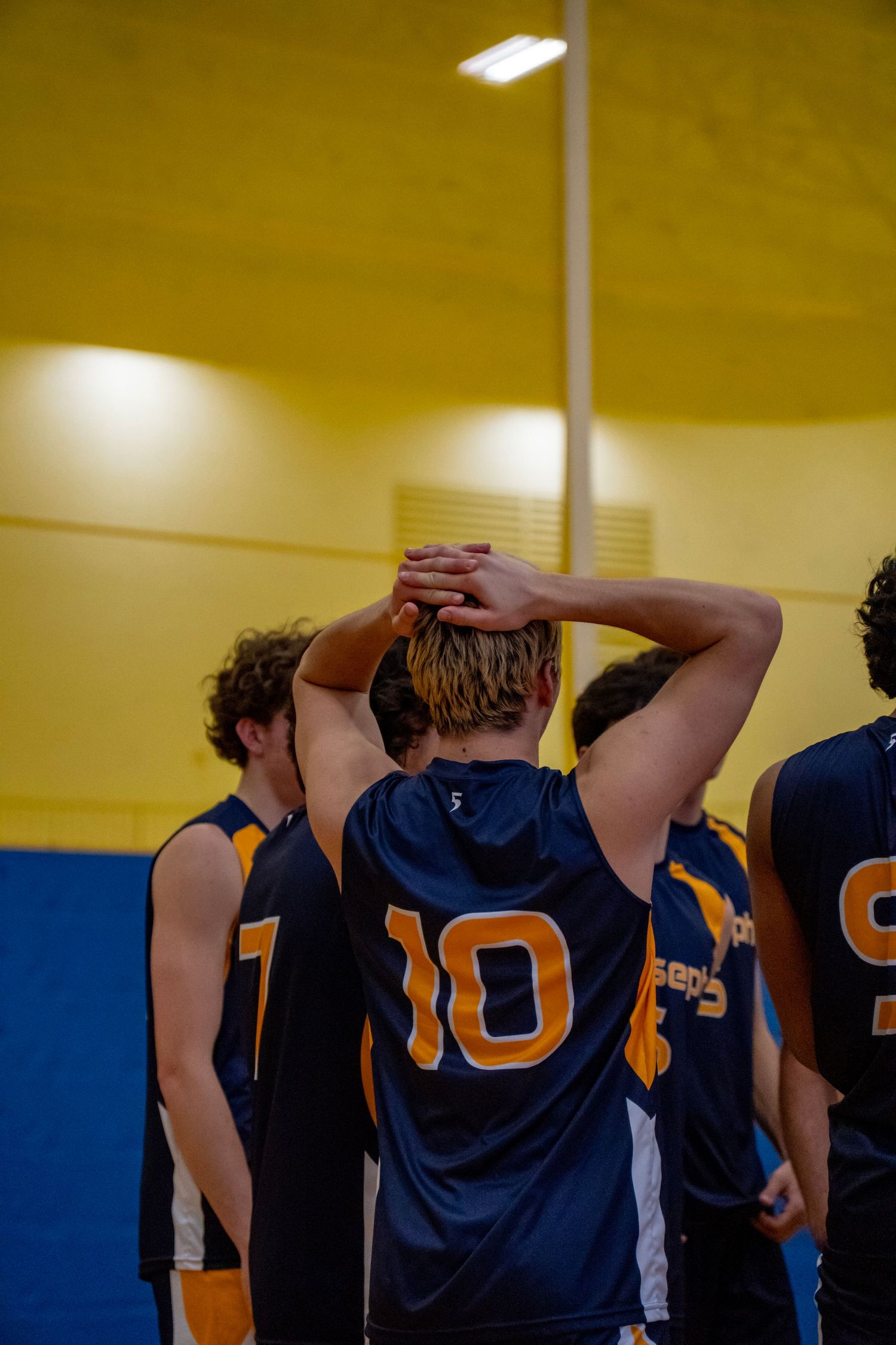 Volleyball teammates huddle together wearing navy blue jerseys during a game break.