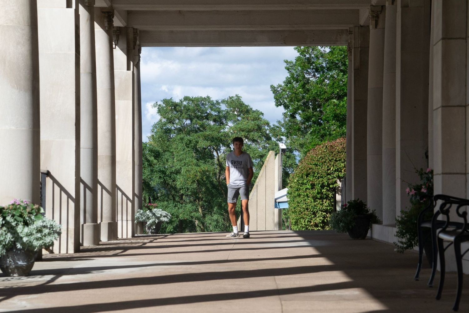 Two figures walking through a covered colonnade with dramatic shadows and pillars.