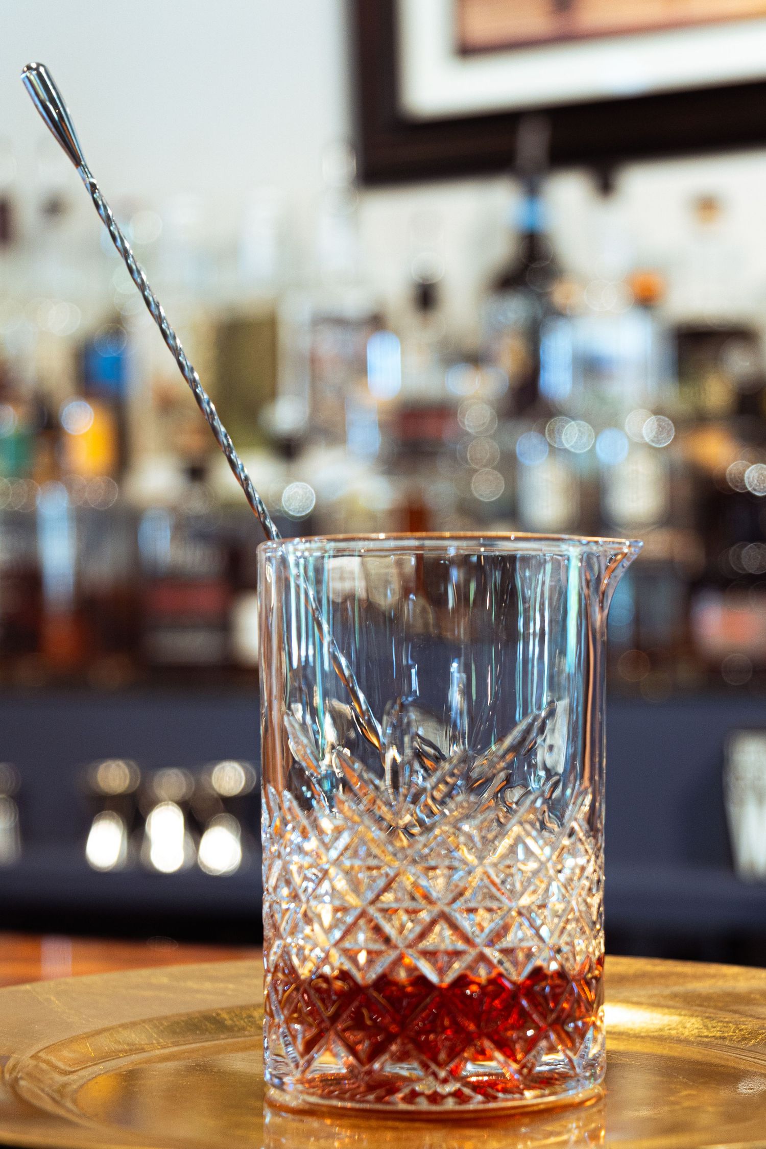 Ornate crystal glass filled with red cocktail syrup and bar spoon on golden tray.