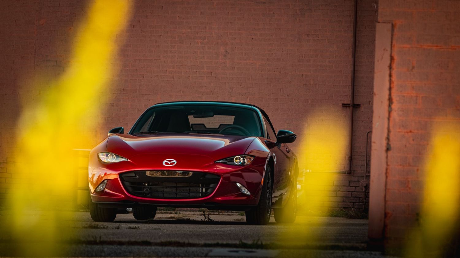 Red performance car captured against brick wall with yellow lighting accents.