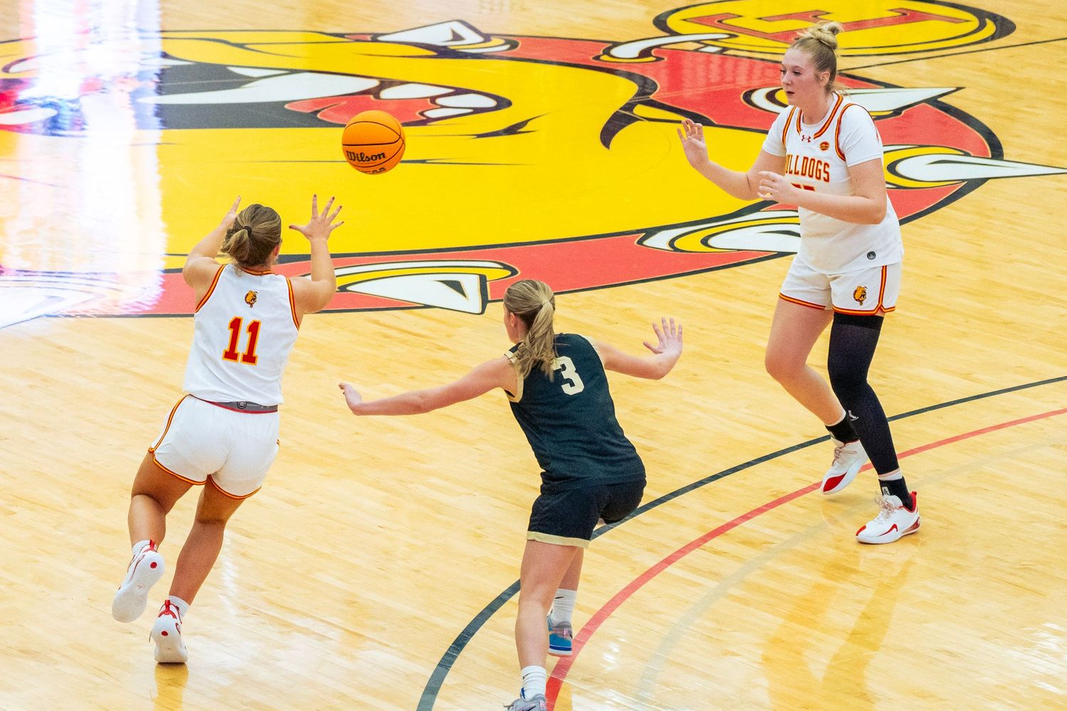 Basketball players compete for possession during an intense game on a bright yellow court with red accents.