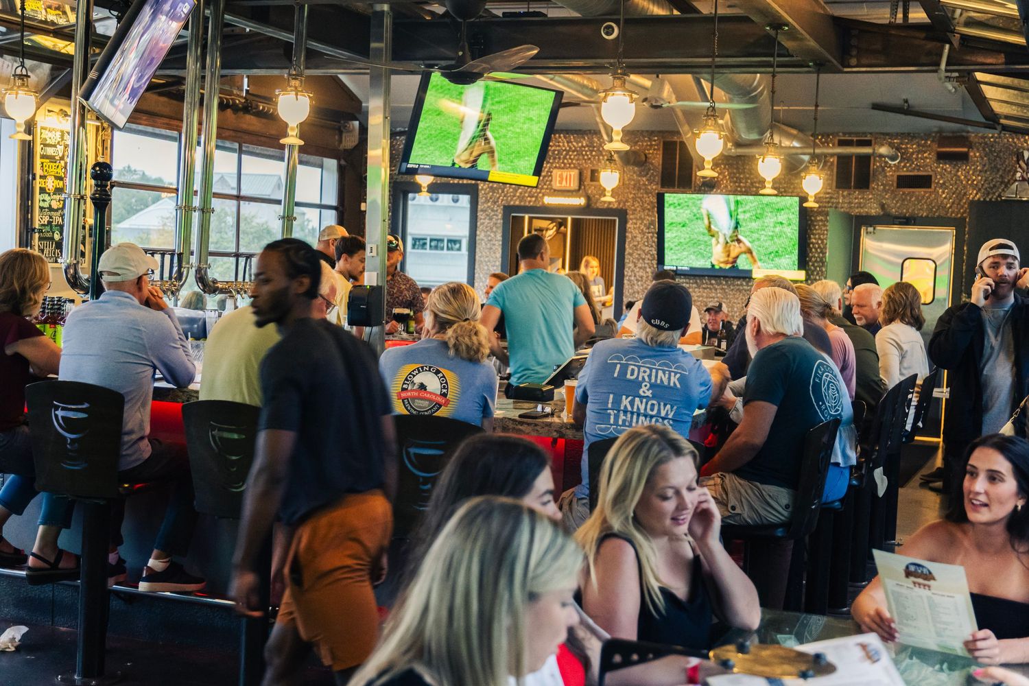 Packed sports bar with customers watching multiple TV screens showing soccer games while enjoying food and drinks.