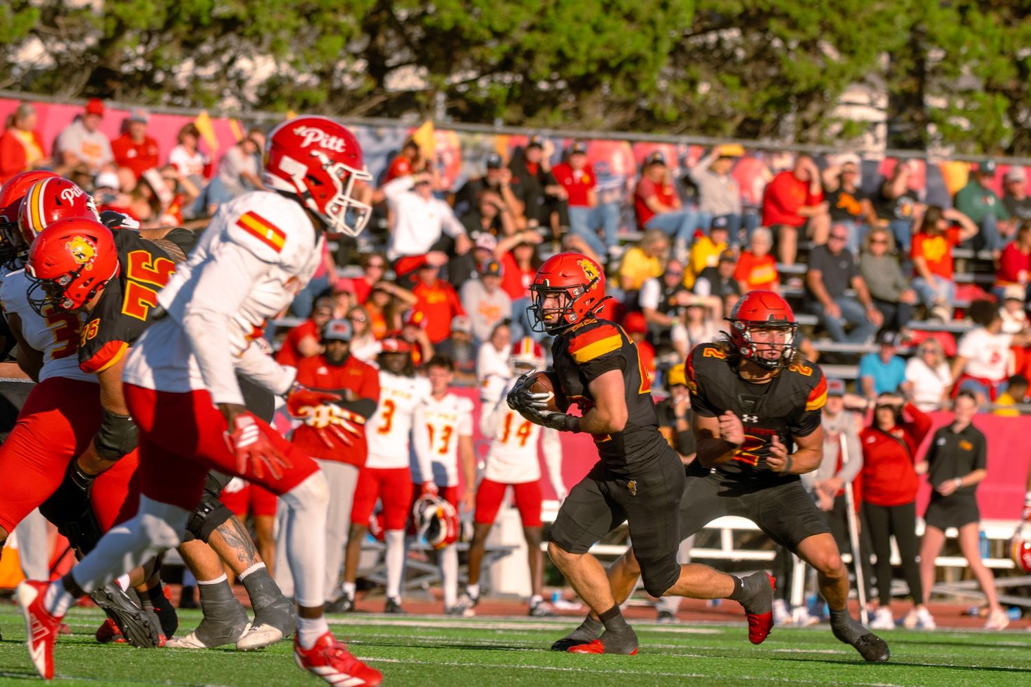 College football players compete during an intense play with a large crowd watching in the stadium background.