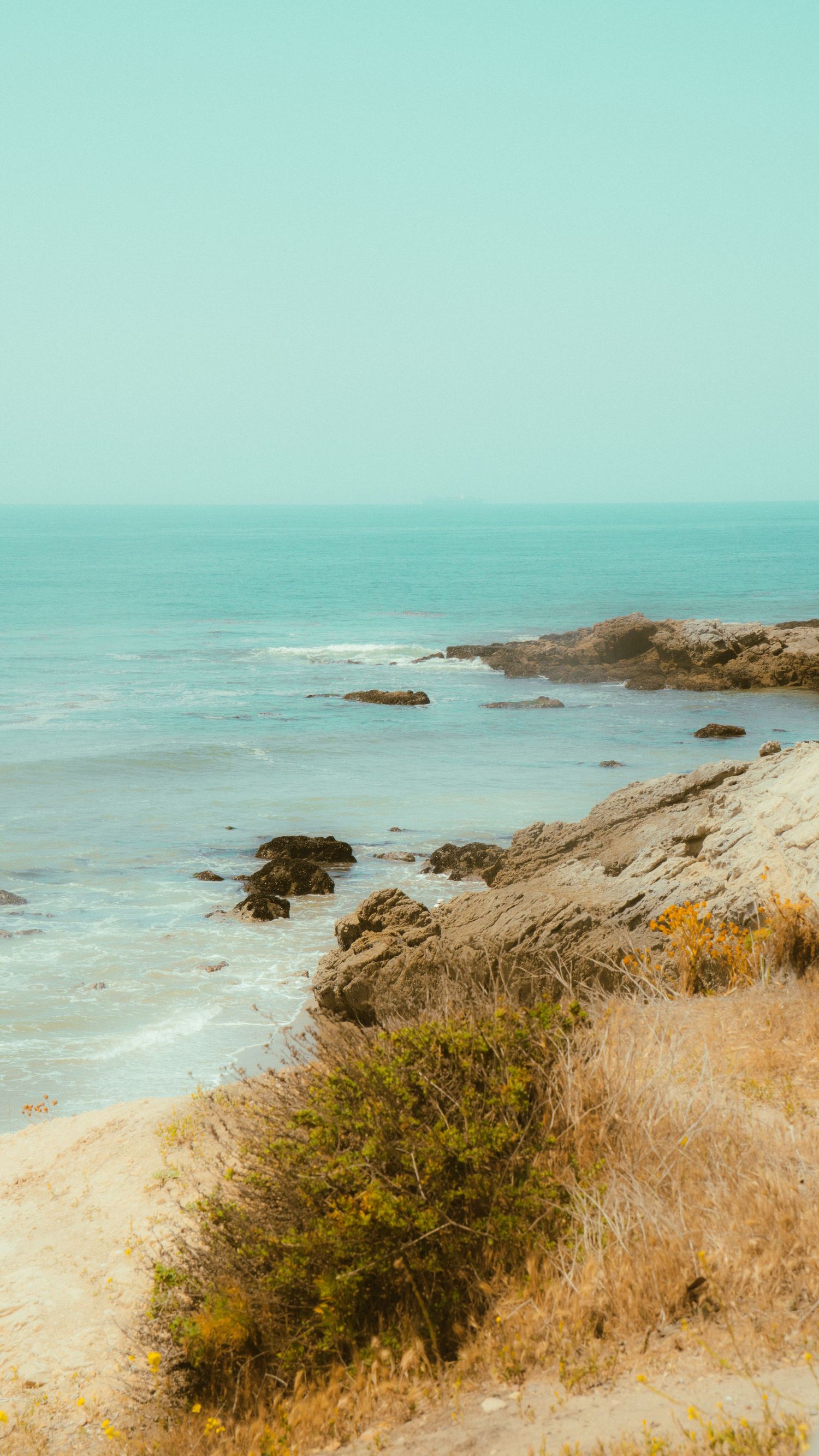Turquoise waters meet rocky coastline with golden vegetation on the cliffs.