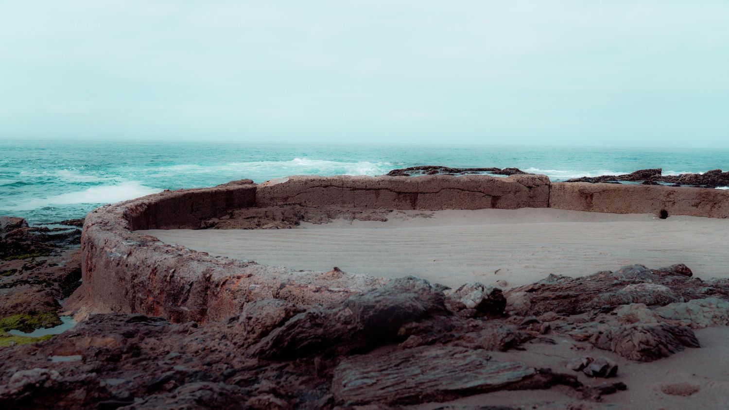 Rocky coastal outcrop with eroded volcanic formations stretching into the misty ocean.