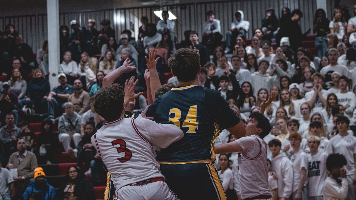 High school basketball players battle for position during competitive game with crowd watching.