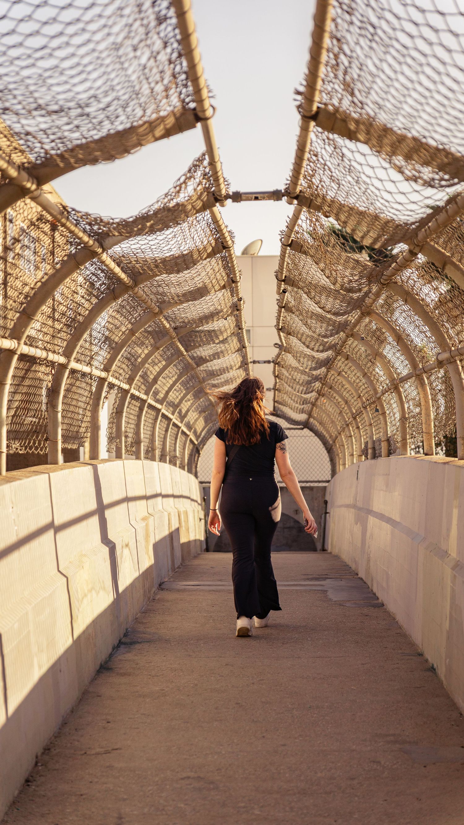 Person walking away in curved architectural passageway with mesh overhead design.