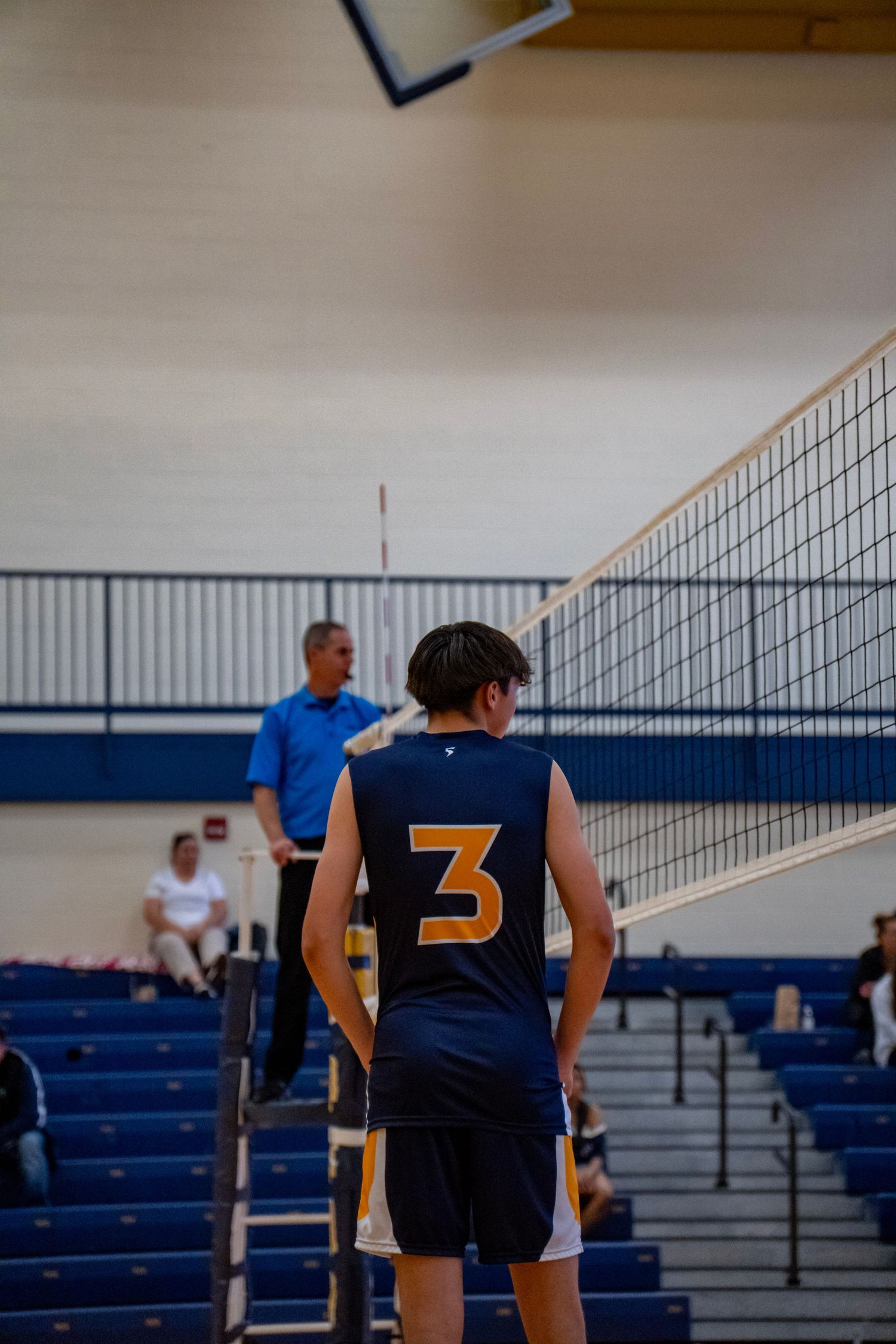 Back view of player wearing jersey number 3 standing at volleyball net during game.
