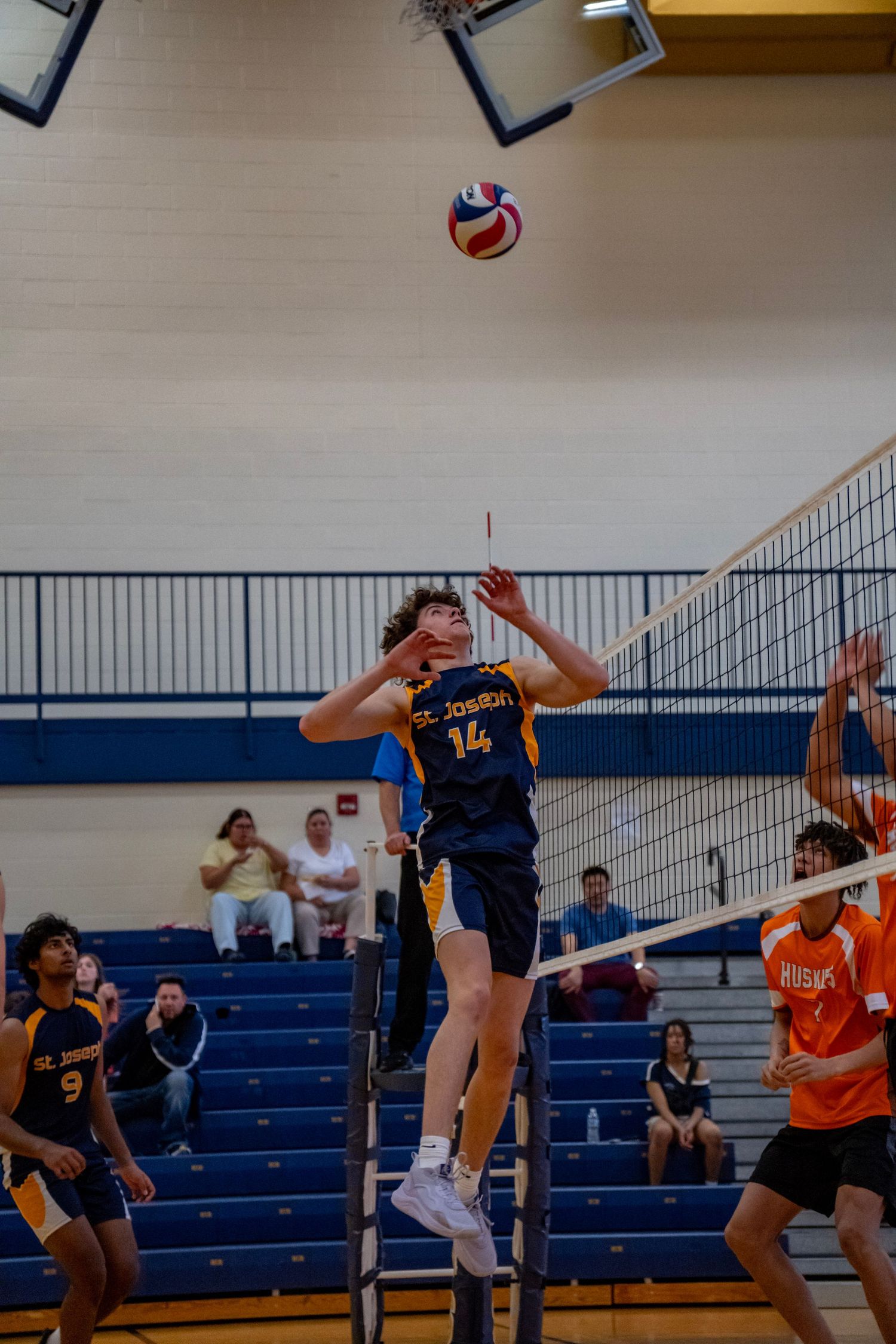 Player jumps to set volleyball during competitive match in indoor gymnasium.