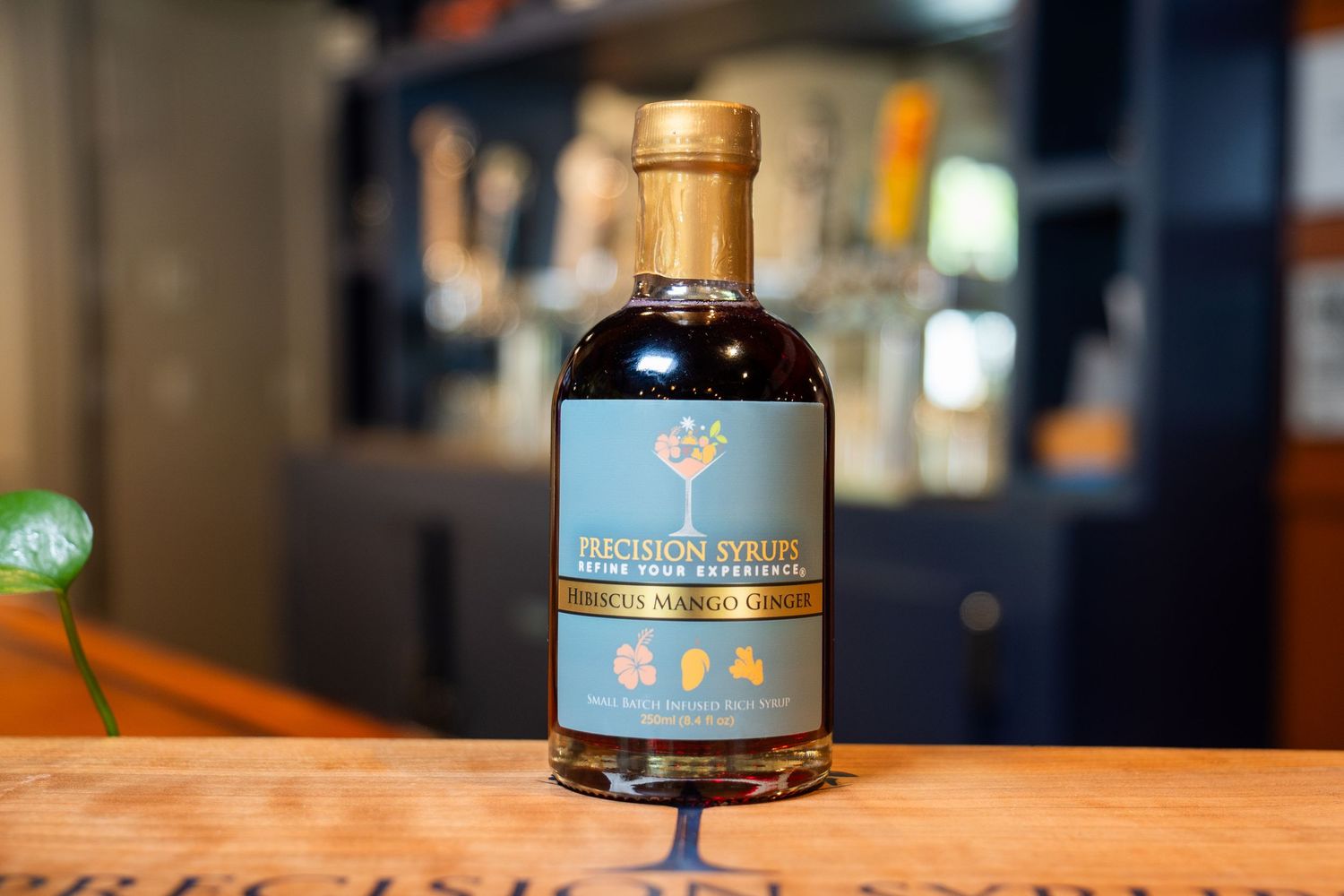 Artisanal cocktail syrup bottle with blue label and gold cap on wooden bar counter.