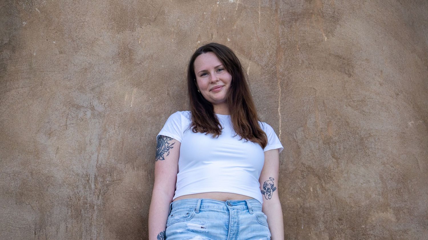 Relaxed portrait against textured wall in crop top and distressed denim shorts.