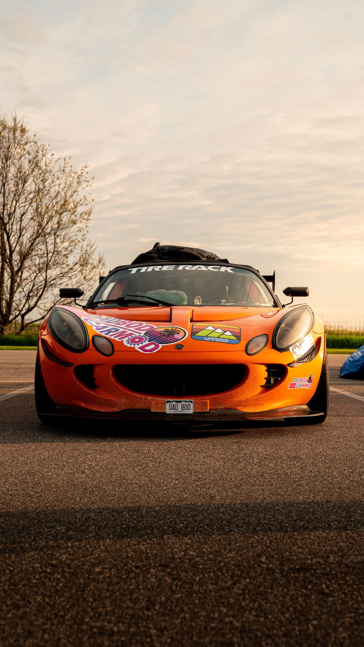 Orange Lotus Elise race car with custom decals photographed at sunset.