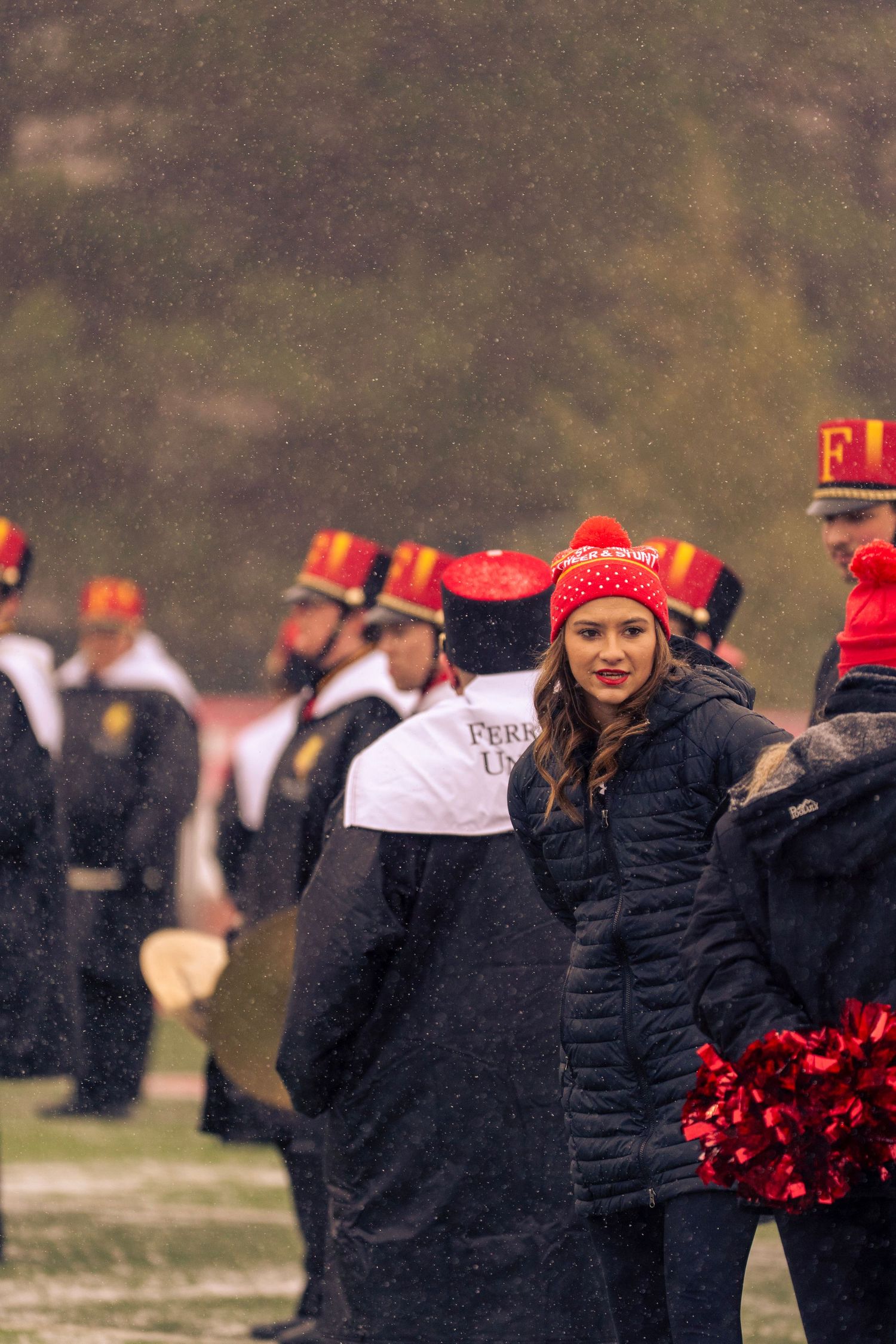High school marching band members in black uniforms and red accessories perform during an outdoor event.