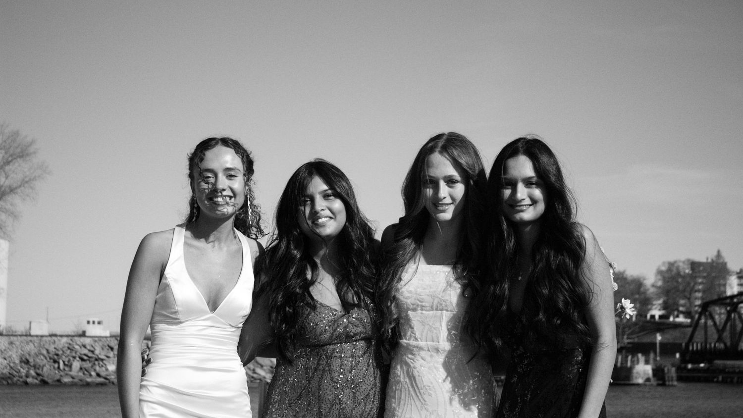 Four people pose together outdoors in black and white, wearing formal dresses with long hair in a happy group photo.