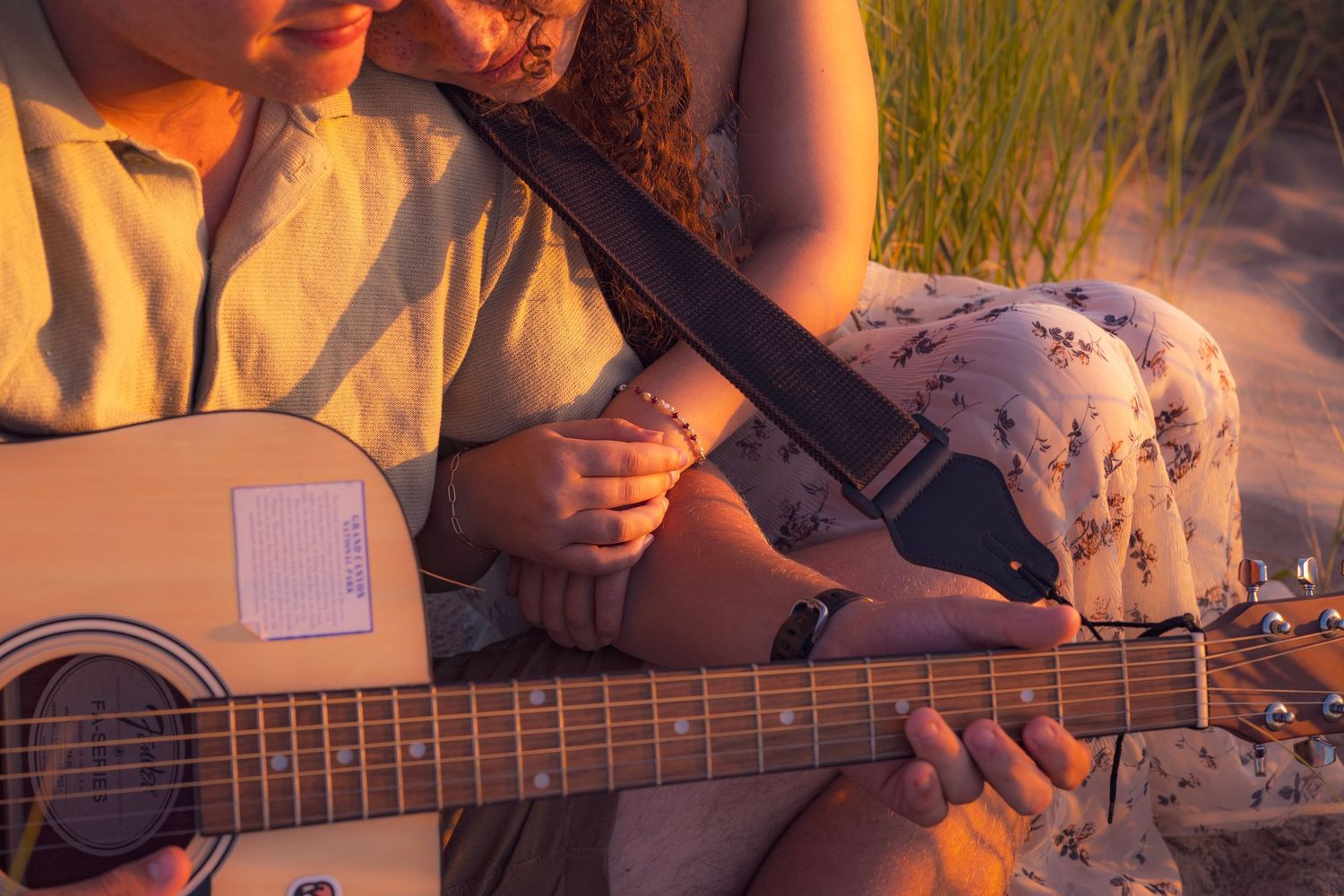 Two people playing acoustic guitar together outdoors in warm sunset lighting.