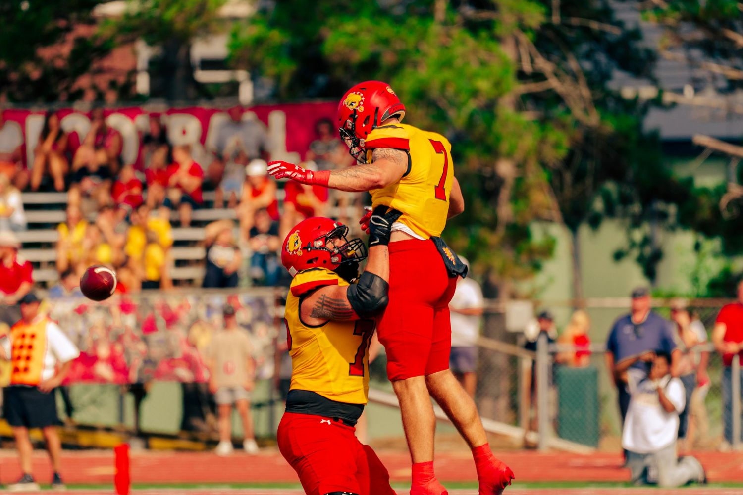 Players in red and yellow uniforms compete for possession during an intense Australian Rules Football match.