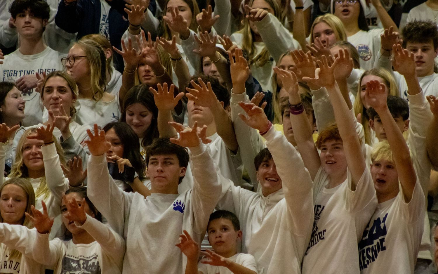 Enthusiastic student section cheers with raised arms during high school basketball game.