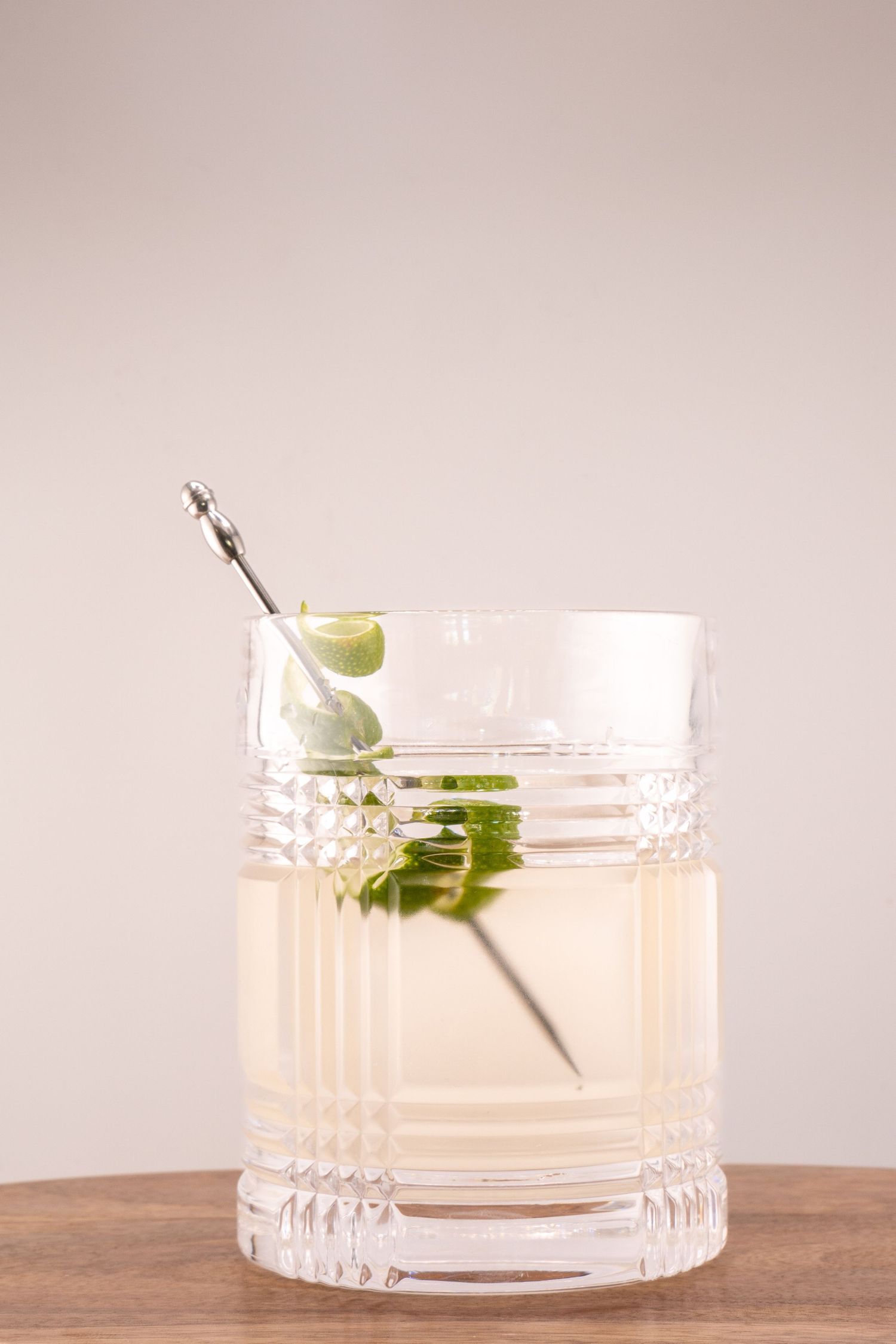 Pale cocktail in cut crystal glass garnished with fresh herbs and metal pick.