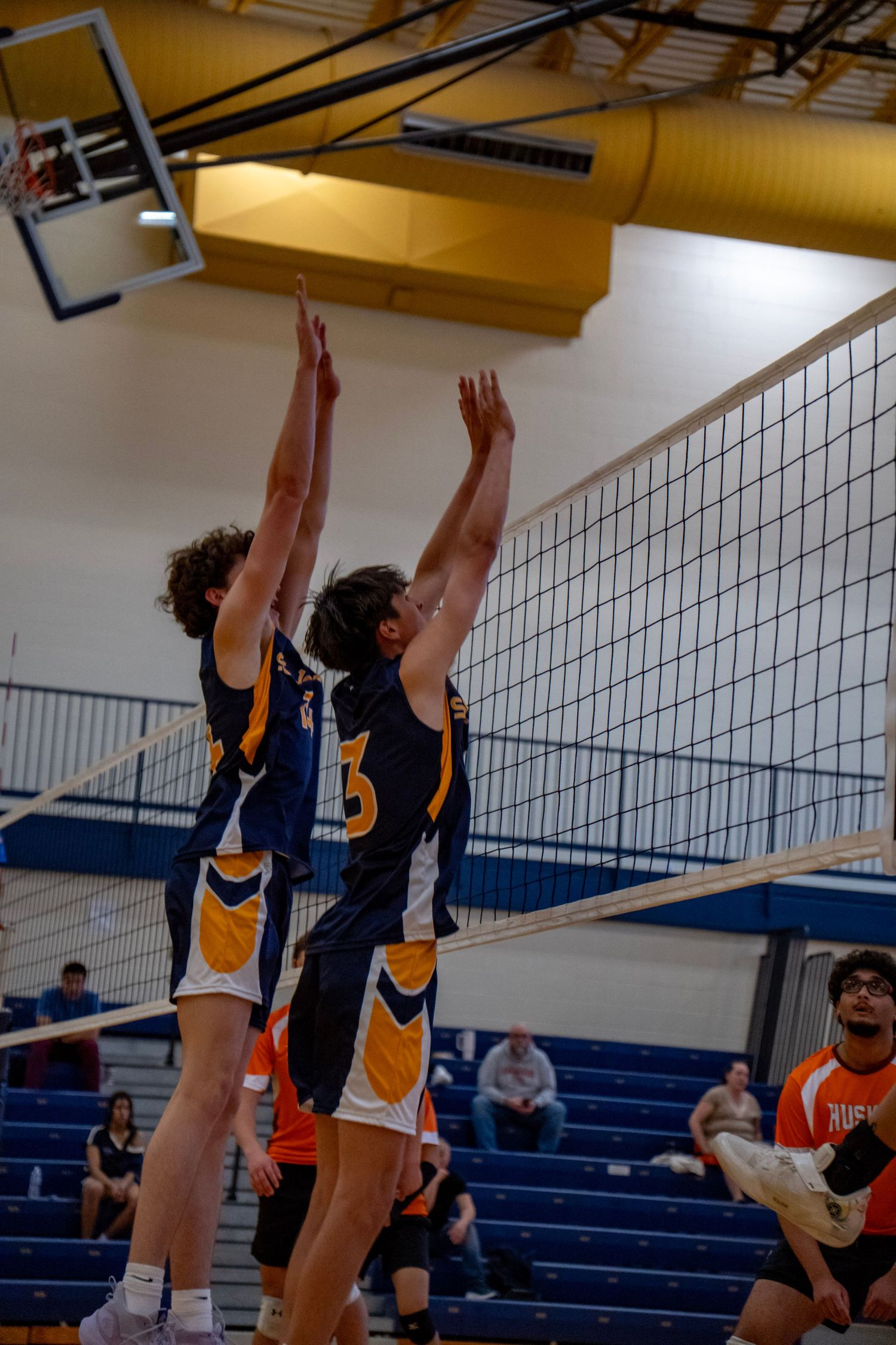 Two teammates jump to block at net during indoor volleyball match.