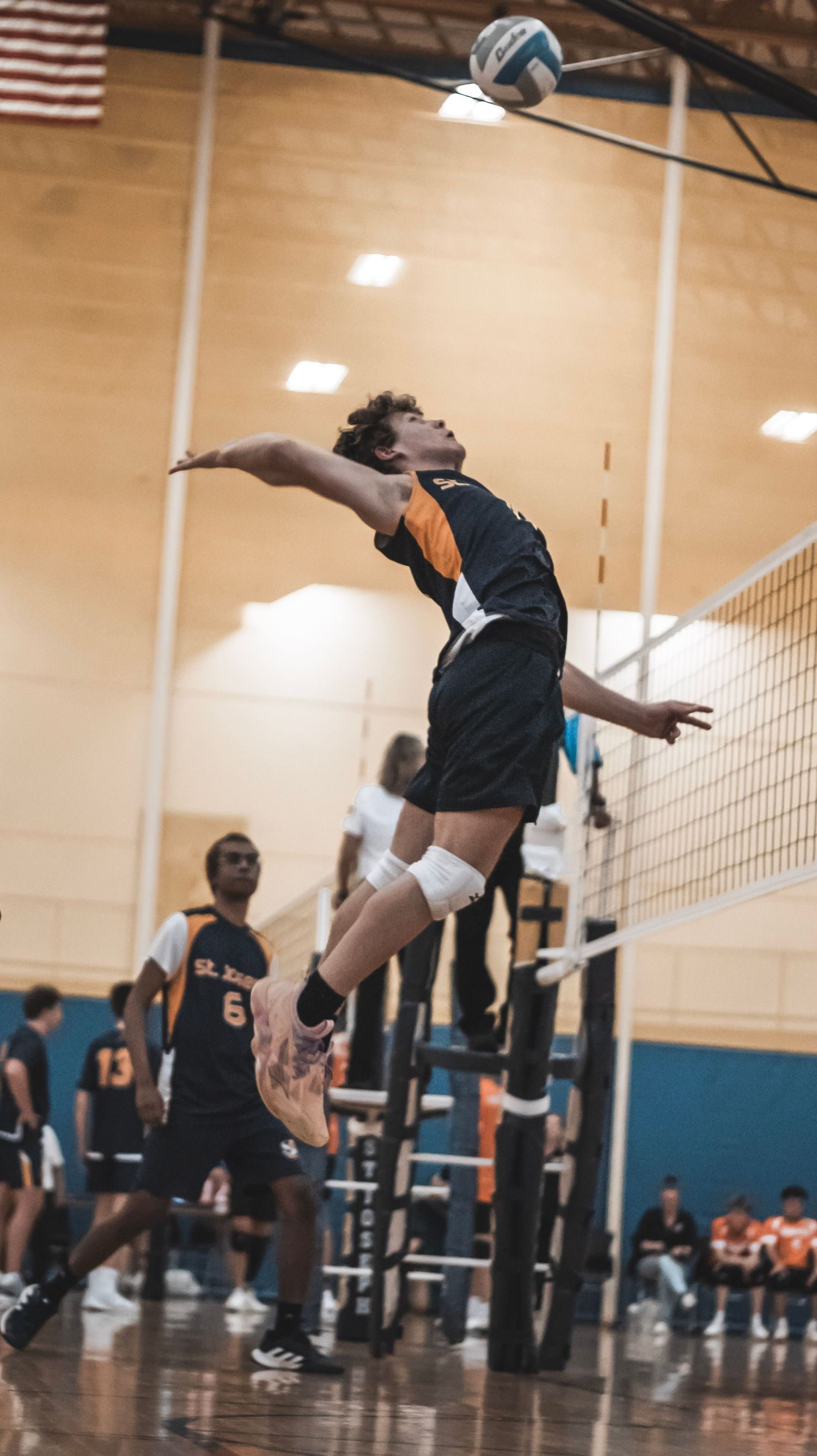 A volleyball player jumps high to serve the ball during an indoor match.