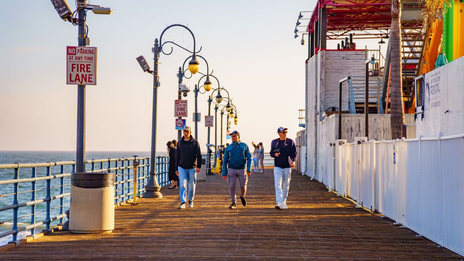 Beachside walkway with lampposts and buildings along the coast during sunset.