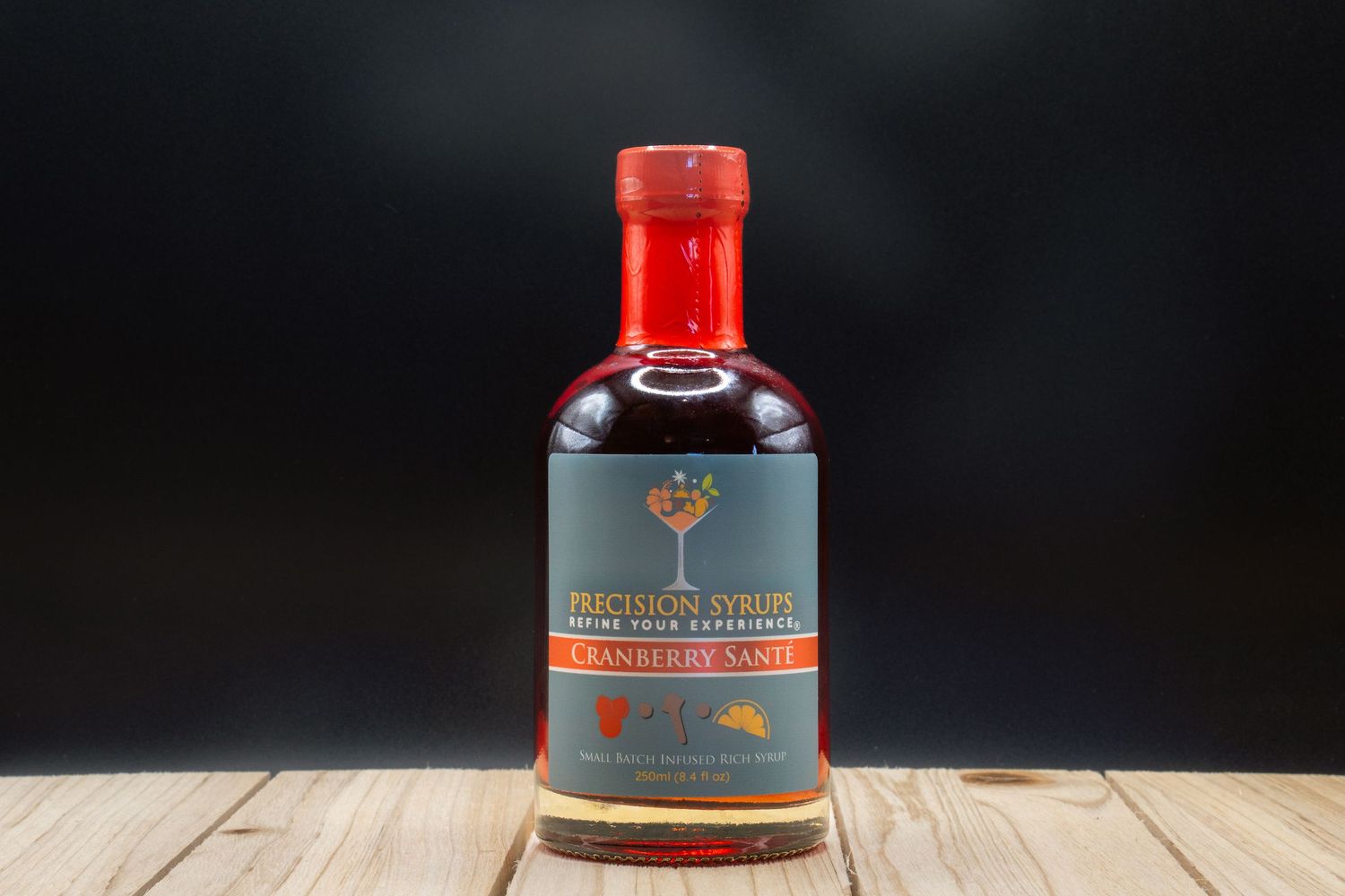 A bottle of cranberry syrup with red cap from Precision Syrups on wooden surface.