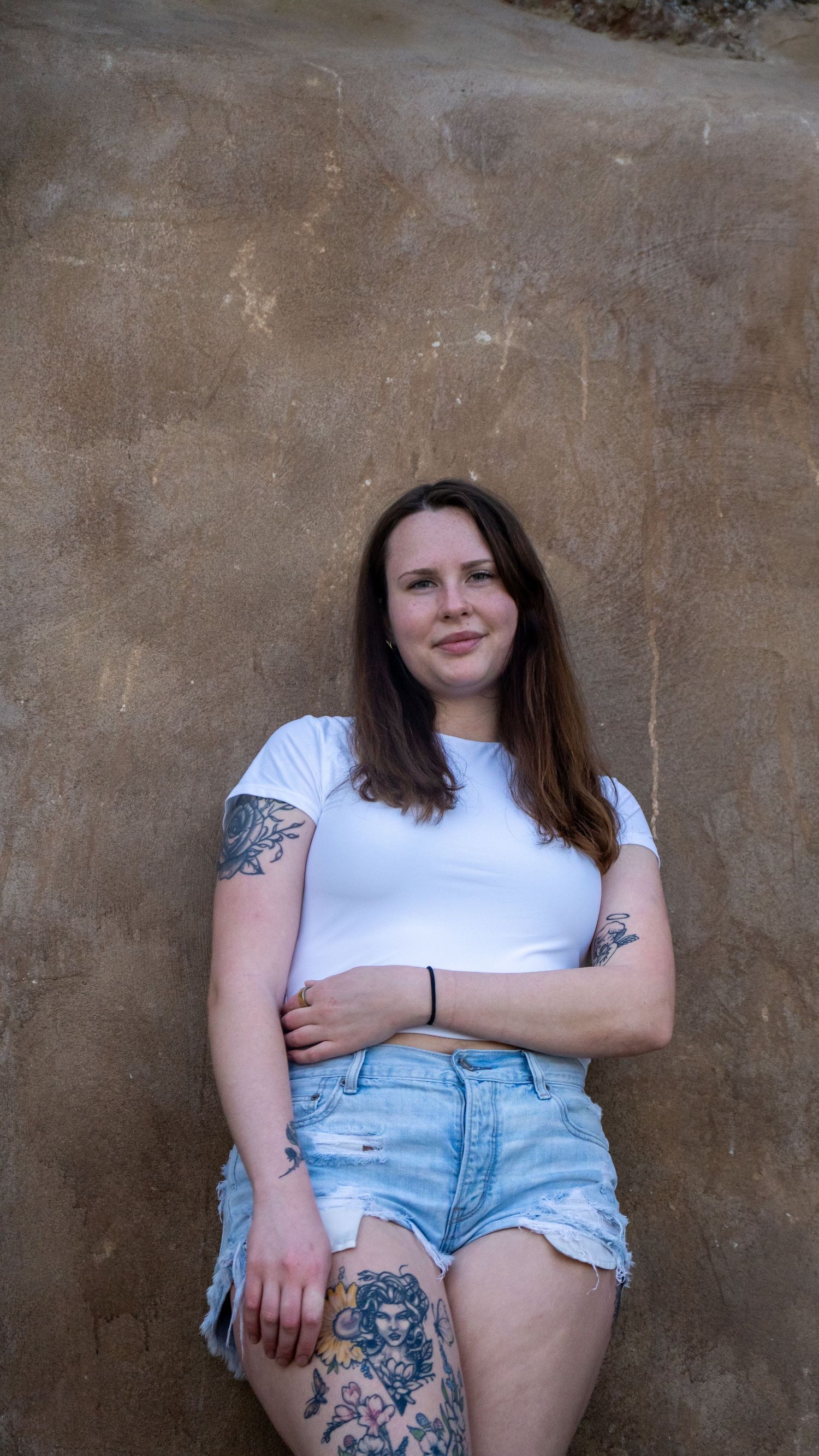 Casual portrait against textured wall showing detailed tattoo artwork and summer style.