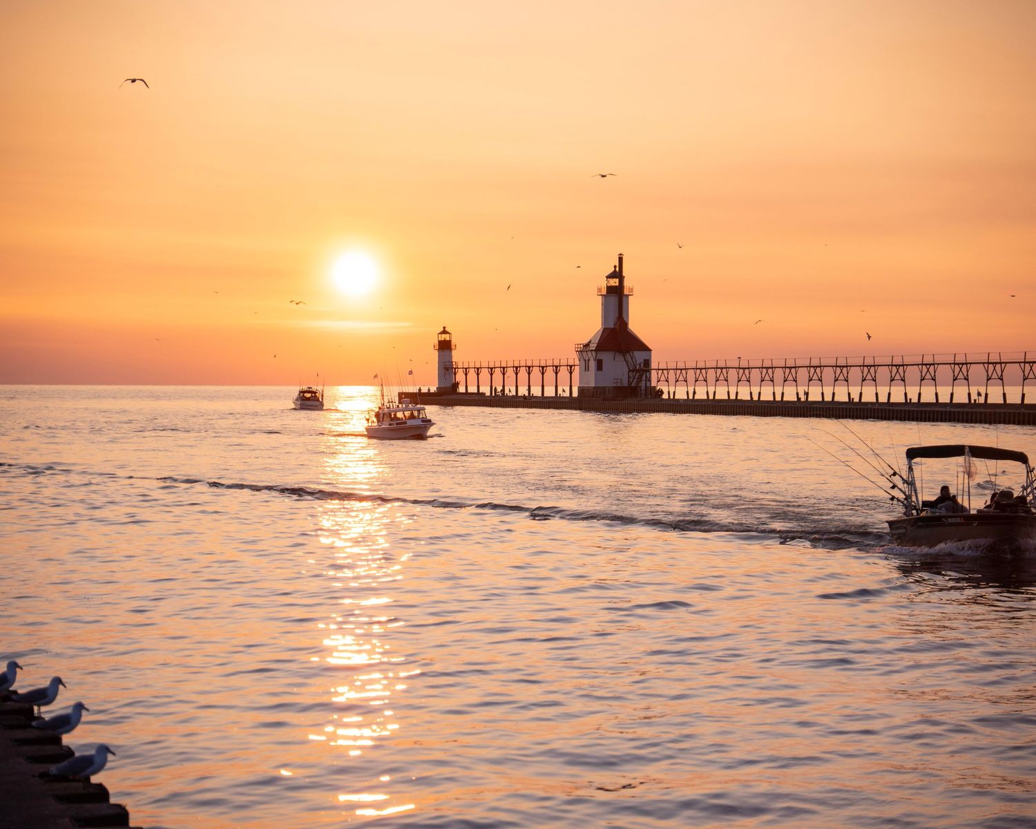 Fishing boats pass near St. Joseph lighthouse during colorful sunset on Lake Michigan.