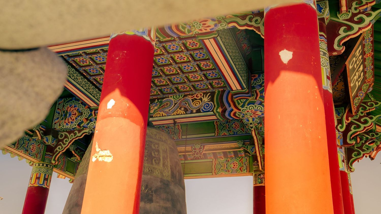 Interior view of Korean temple showing red pillars and decorated ceiling with traditional patterns.