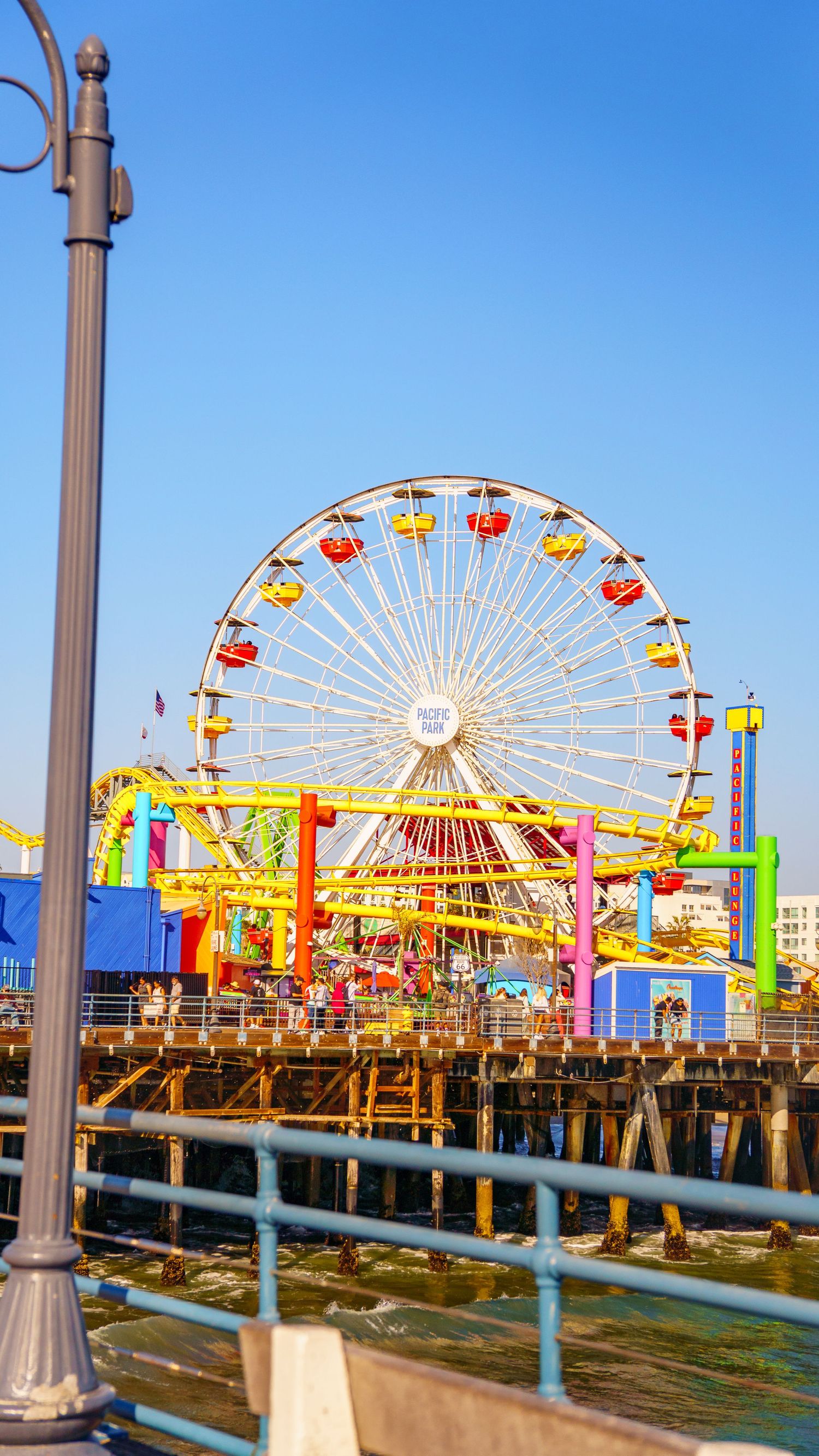 Colorful Ferris wheel and amusement rides on Santa Monica Pier against blue sky.