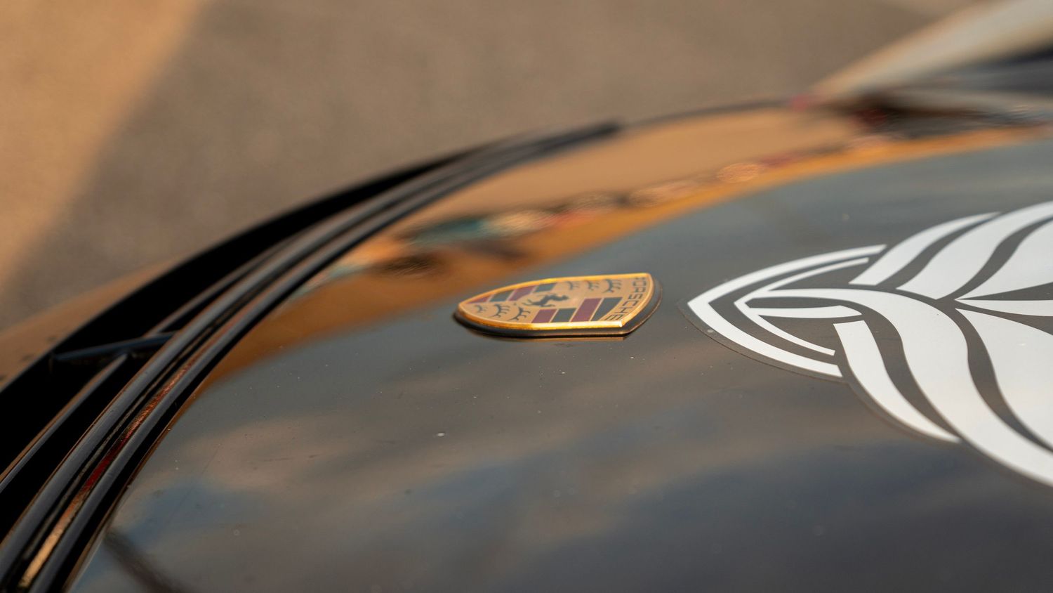 Macro shot of Lotus badge and racing stripes on black car hood.