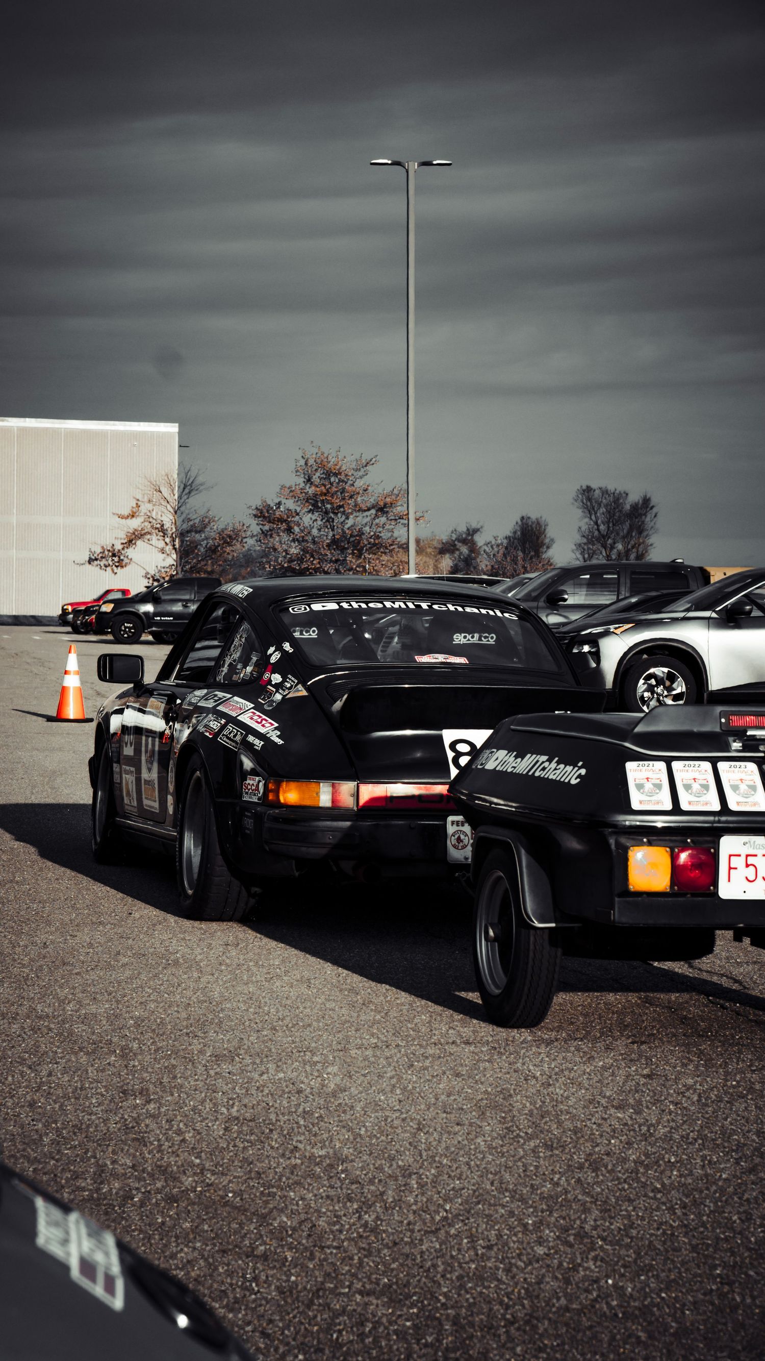 Black vintage Porsche sports cars lined up at a car show under dramatic stormy skies.