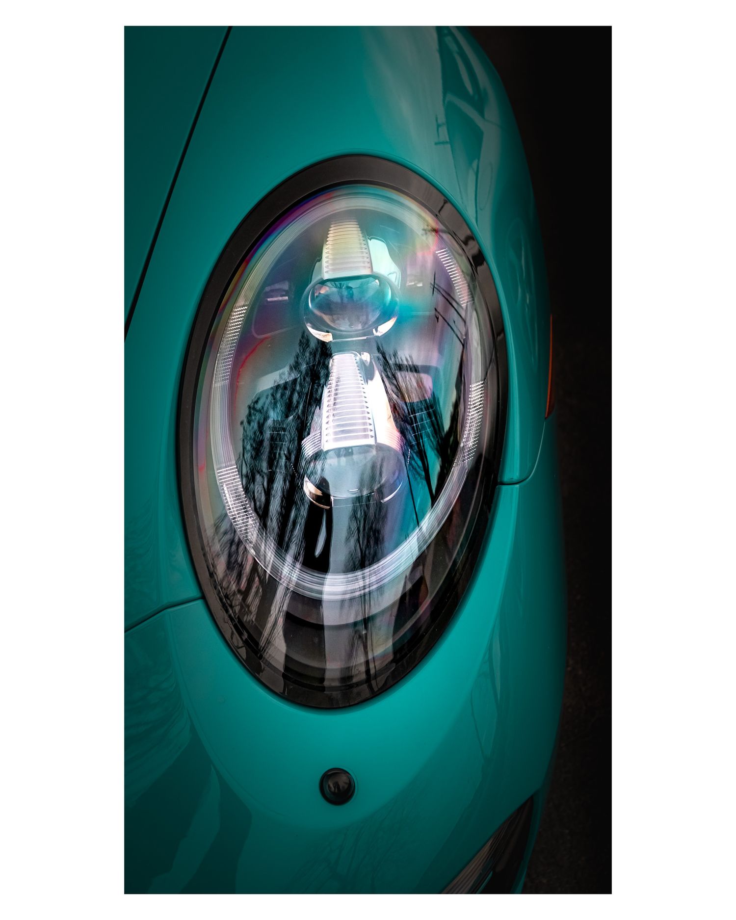 Close-up of a turquoise Porsche's rounded headlight with LED lighting elements.